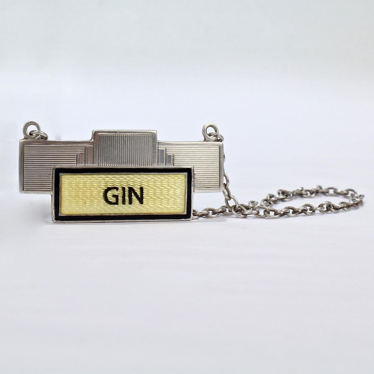 A wonderful Art Deco period English sterling silver Gin bottle label. Perfect for the Modern Bar!

With black and yellow enamel, this sterling silver label has etched decoration to the top and is complete with its original link chain.

The reverse