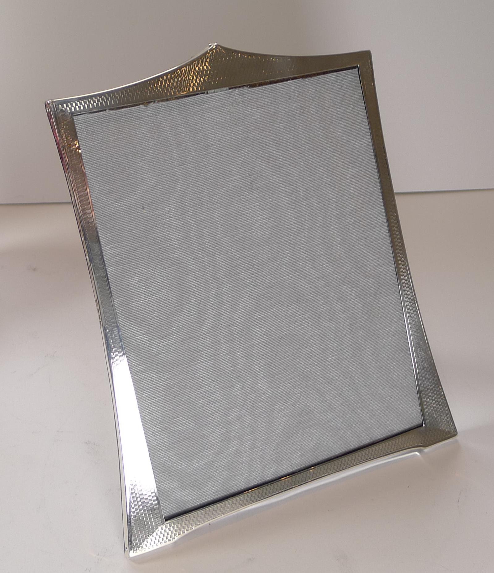 A handsome large Art Deco photograph frame, the silver having an all-over engine turned decoration. The silver is fully hallmarked for Birmingham 1928.

The back is made from solid oak with a hinged folding easel stand.

Excellent condition