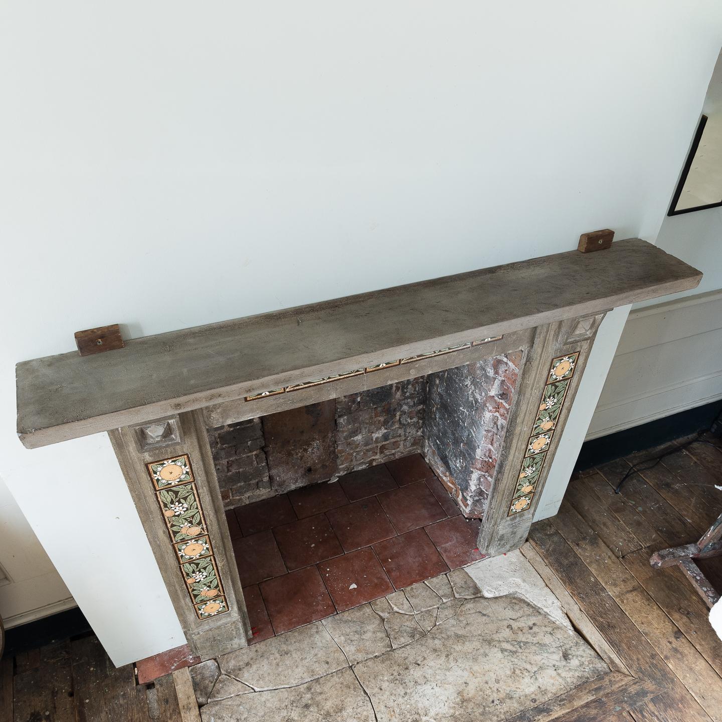An English Arts & Crafts artificial stone and tiled fireplace, late 19th century, the rectangular shelf supported by stylised Gothic corbels, the frieze and jambs with inset tiles in the manner of May Morris, on plain footblocks.
  