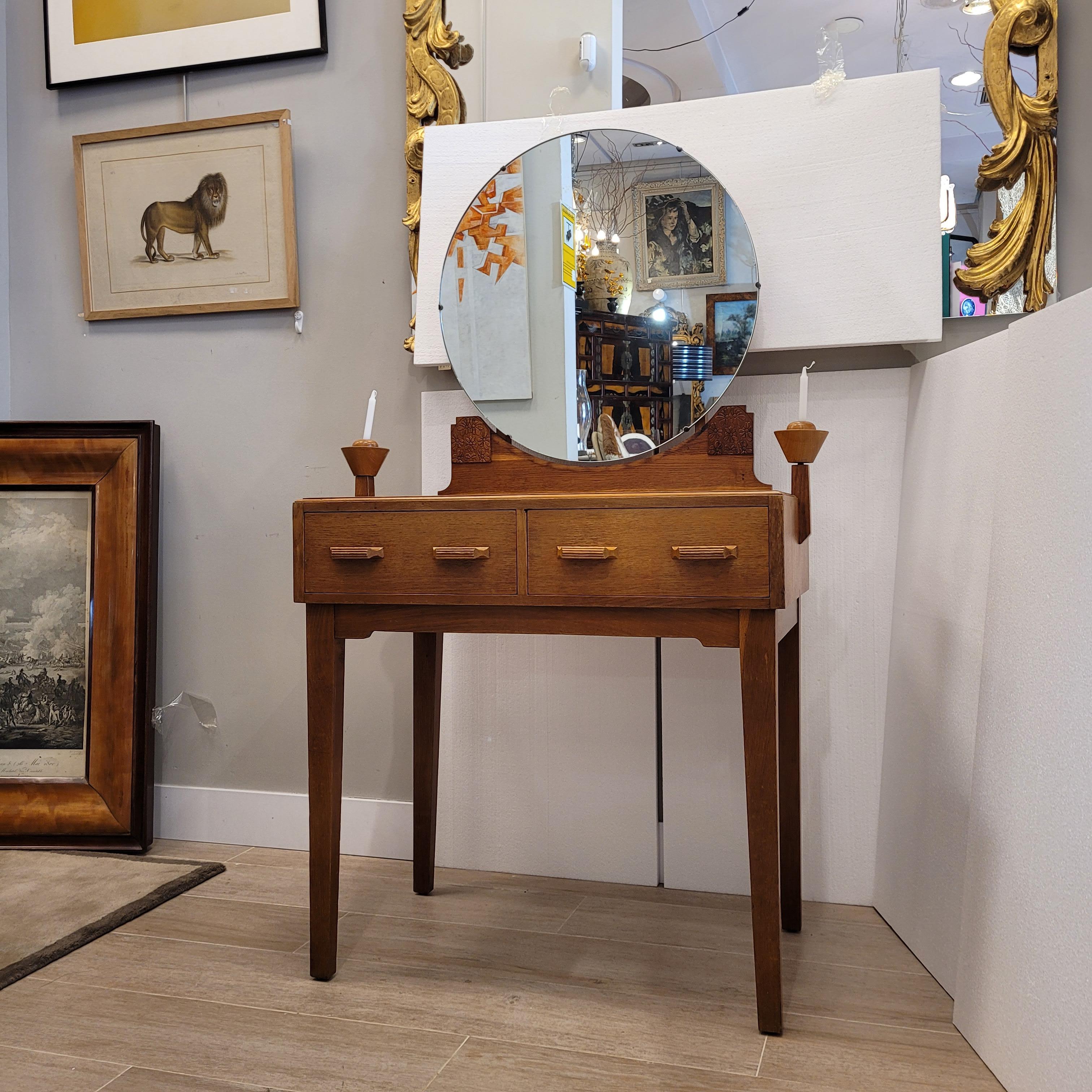 Delightful  and beautiful dressing table and desk in oak wood in the Arts and Crafts style produced in England. This piece has a base on which a circular frameless mirror stands, resting on a carved wooden support with floral decorations. It has two