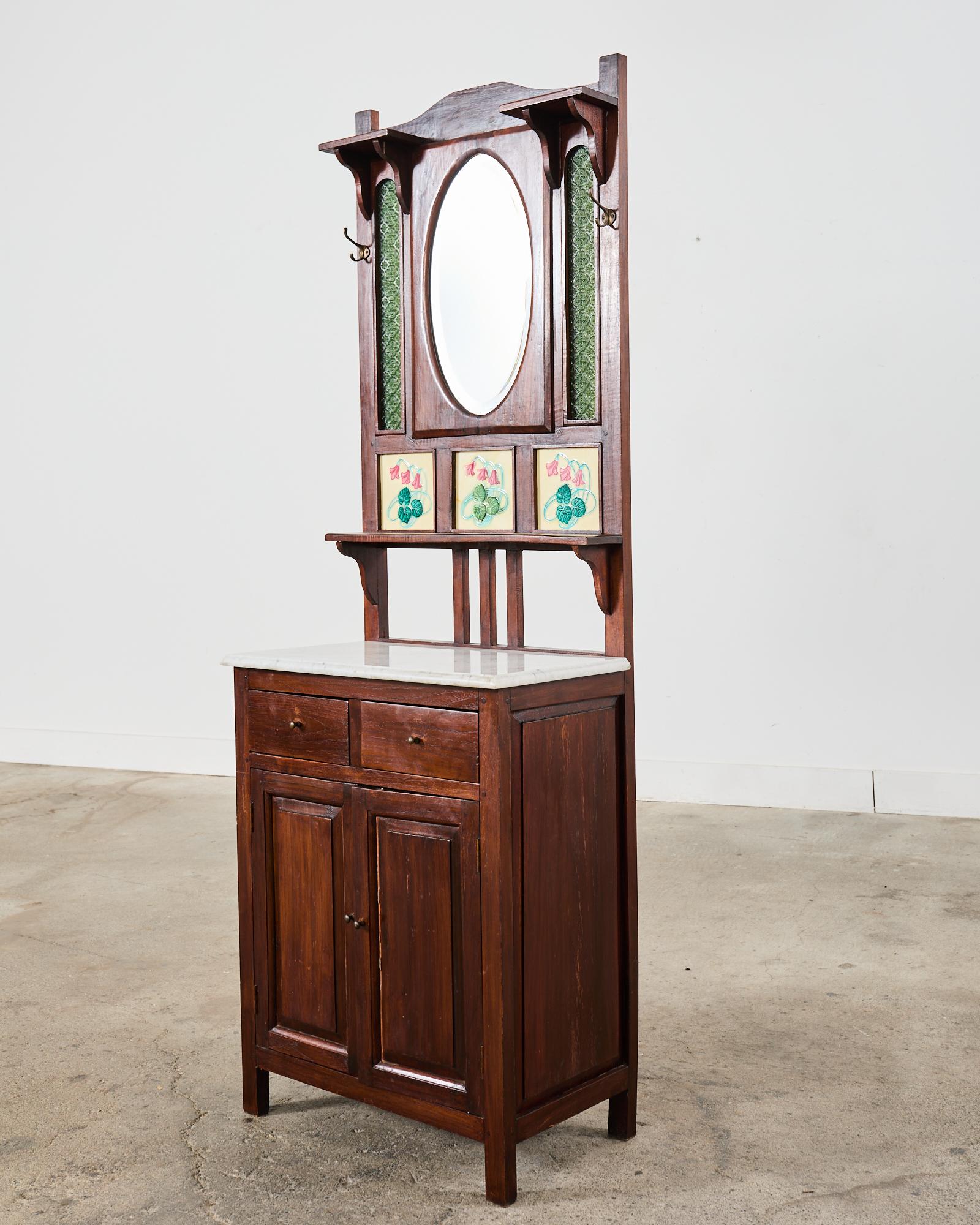 Extraordinary mirrored hall tree with brass hardware and inset with colorful Art Nouveau floral tiles. Featuring a white marble slab surmounting an attractive craftsman style storage cabinet. The mirror is of fine quality with a large bevel. Each