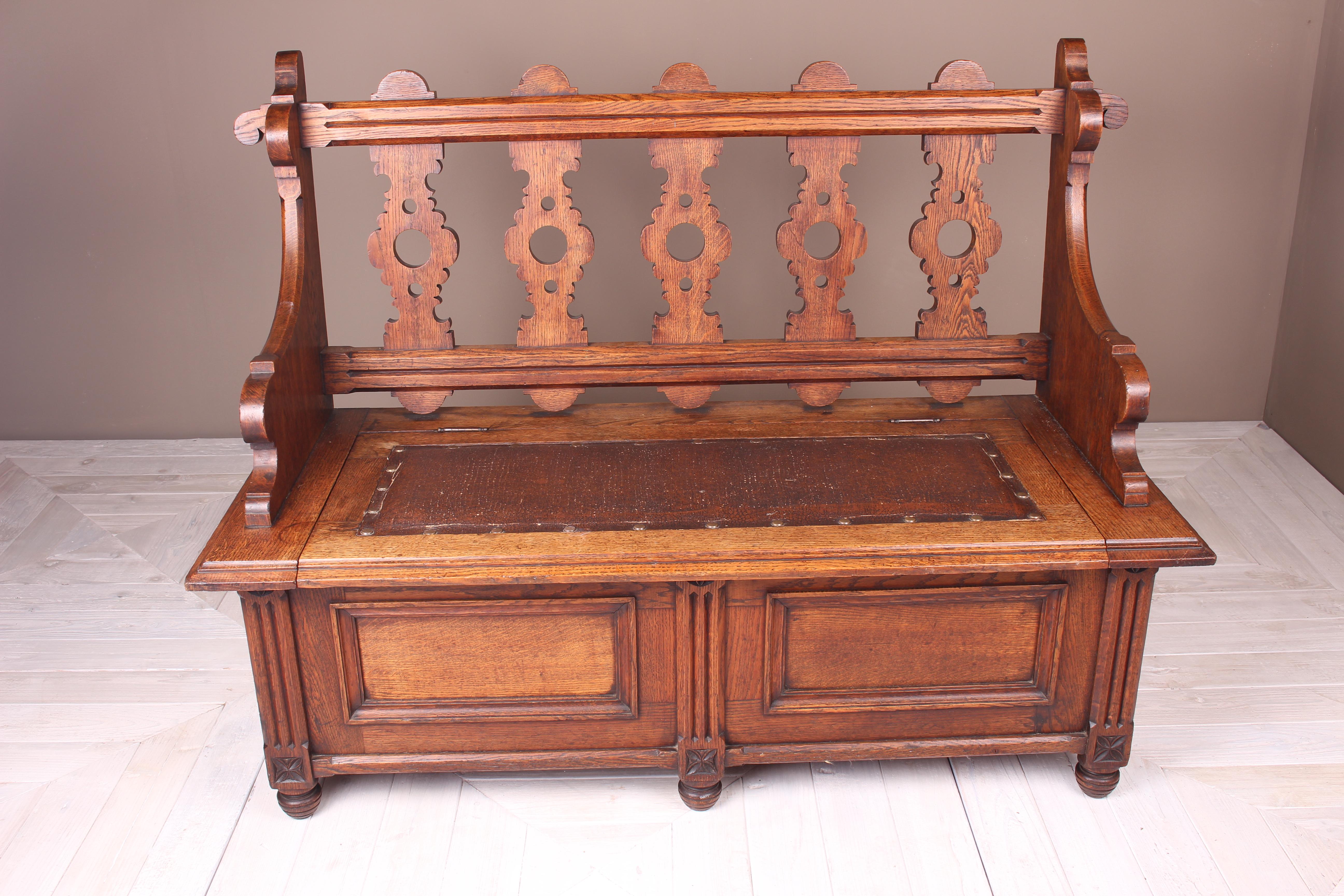 An attractive Arts and Crafts oak hall seat or settle. Having a box base with studded leather seat and pierced splats to the back. The front section with adjacent fielded panels separated by three fluted columns, each having stylized decorative