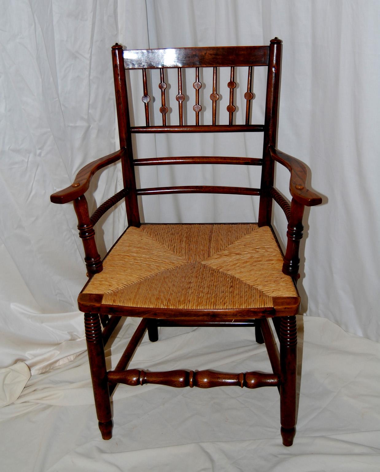  English Arts and Crafts period elm rush seated spindle back armchair.  This armchair has unusual flattened turnings to the back and bobbin turnings on the member under the arm.  The double box stretchers connecting the legs make for a sturdy yet