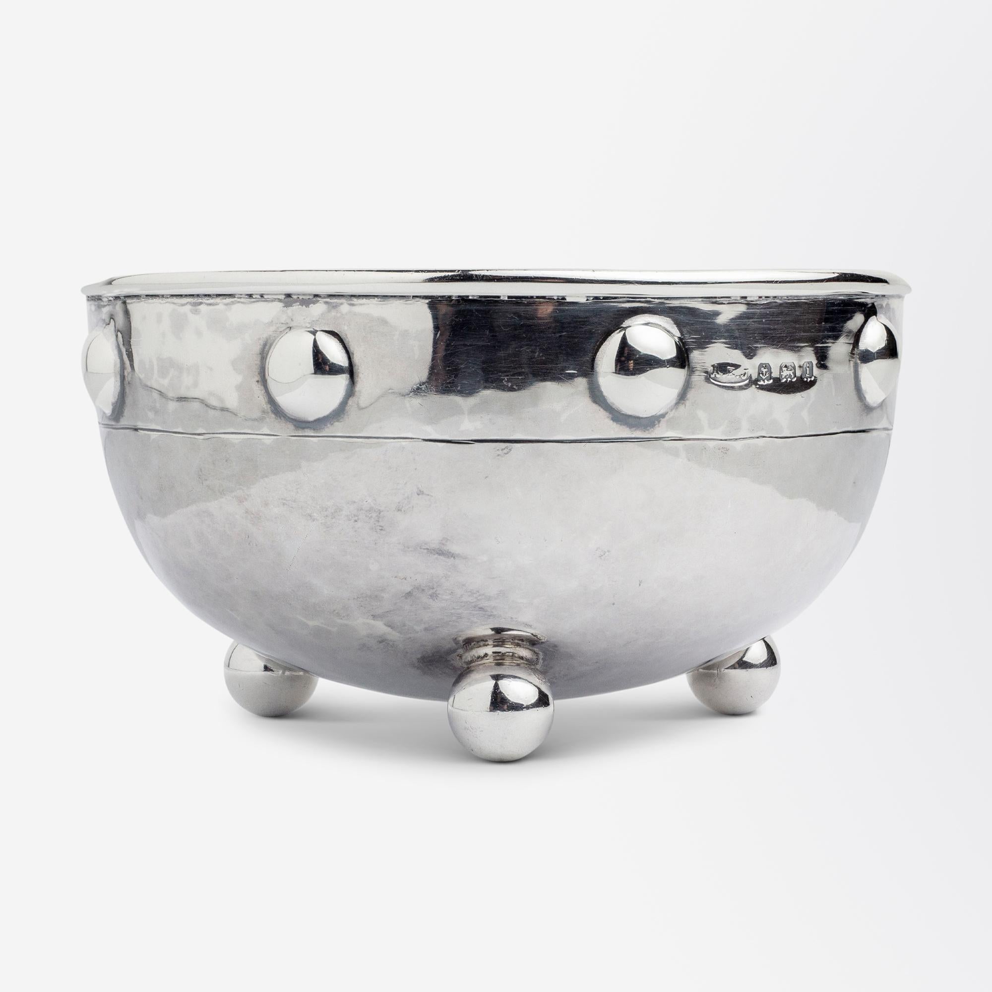 A small, hand-wrought, sterling silver, Arts & Crafts era bowl by English silversmith Albert Edward Jones (1878-1954). The bowl which is minimal in its decoration sits atop of three sterling silver ball feet and features a rim of silver buttons. The