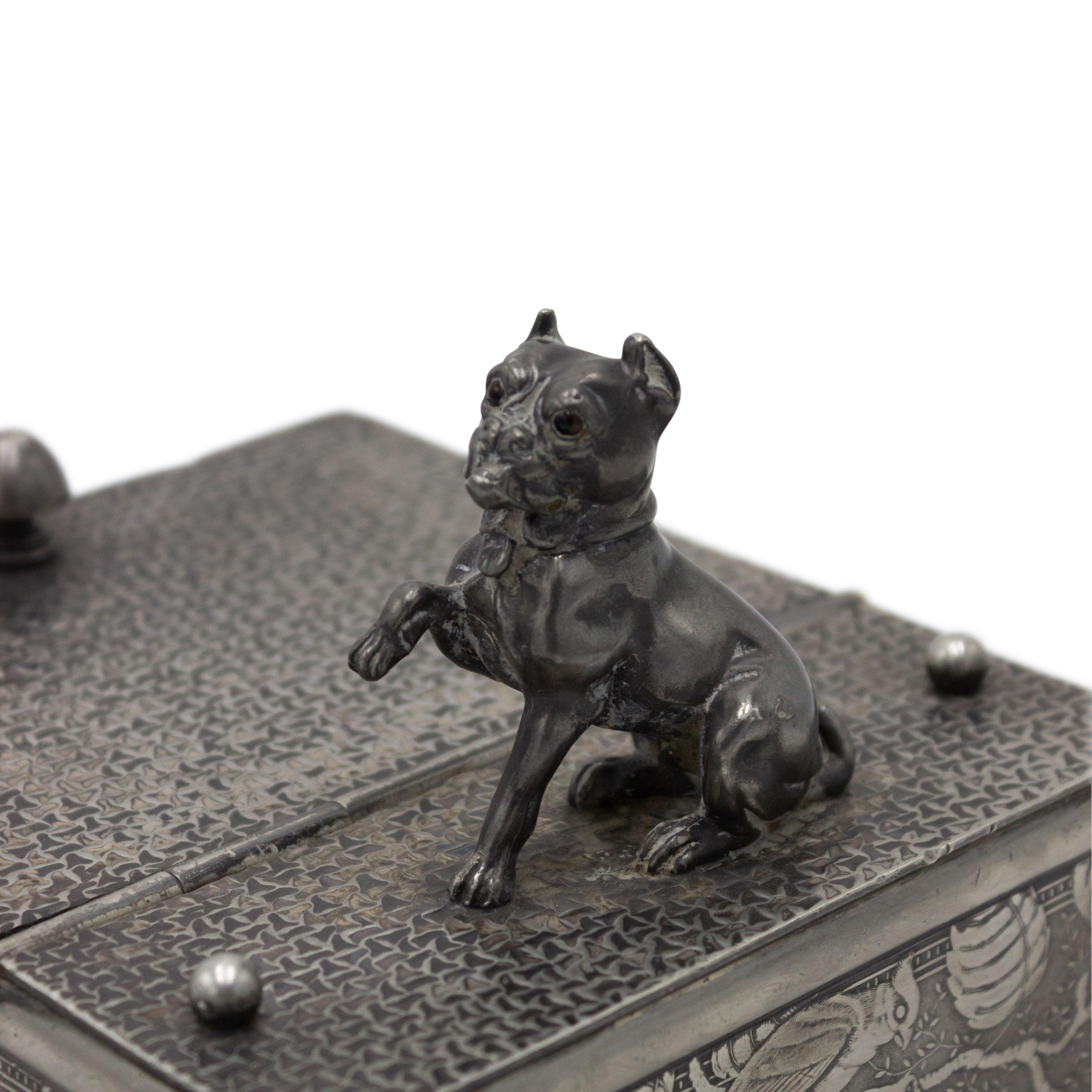 English Arts & Crafts pewter box with a floral & bird design and figure of a dog on top.
  