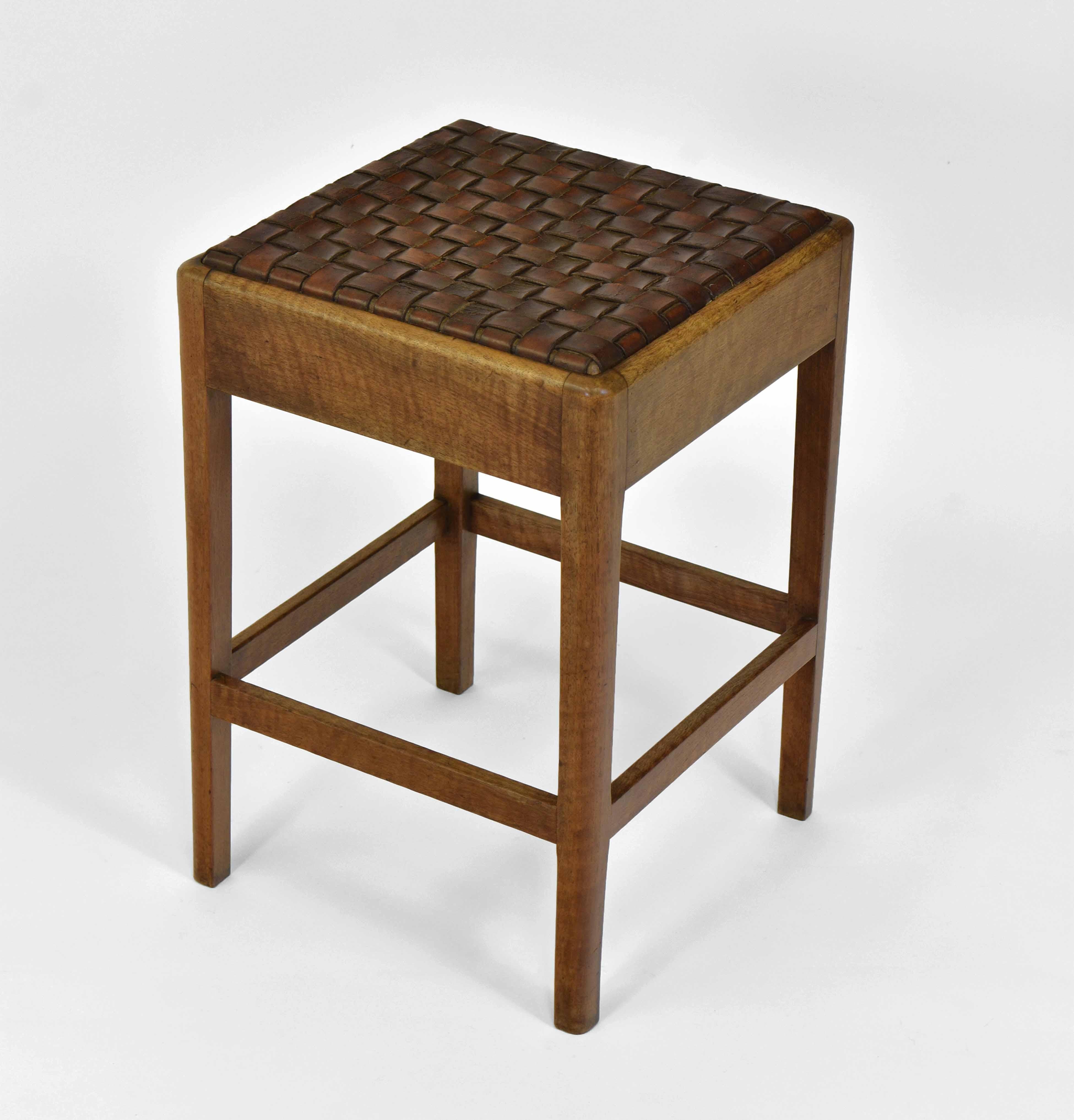 An Arts & Crafts Cotswold School manner walnut and leather lattice strapwork topped stool. Circa 1920. Paper label 