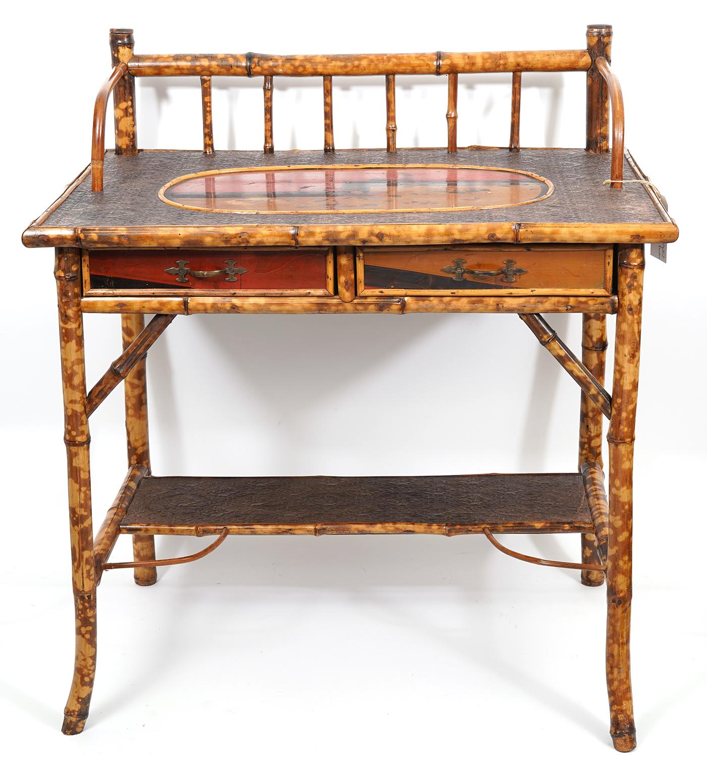 This early 20th century English bamboo writing desk features an embossed leather lined top centering an oval Zen style lacquered image with birds and blossoming plants above two similarly japanned fronted drawers. The slightly splayed legs are