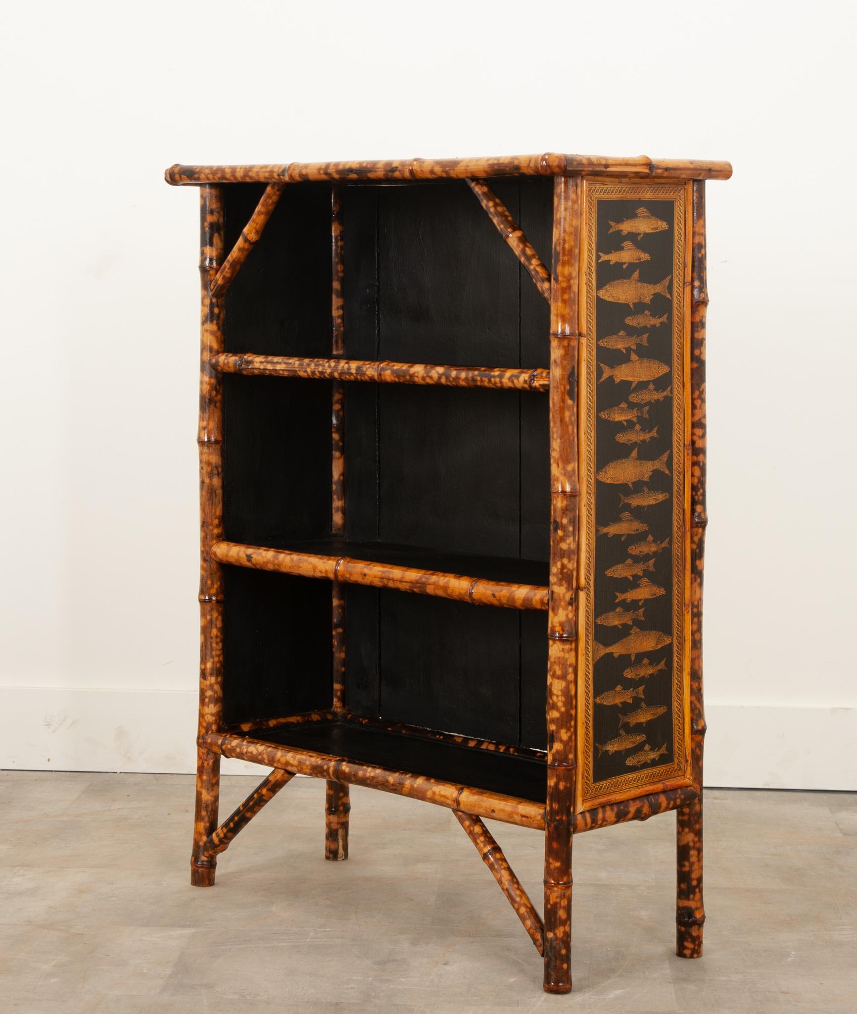 A bamboo bookcase, made in England at the end of the 19th century. The shelves were once topped with woven seagrass that has been removed due to excess wear. It has been replaced with fresh black paint and brilliant découpage paper fish and styled