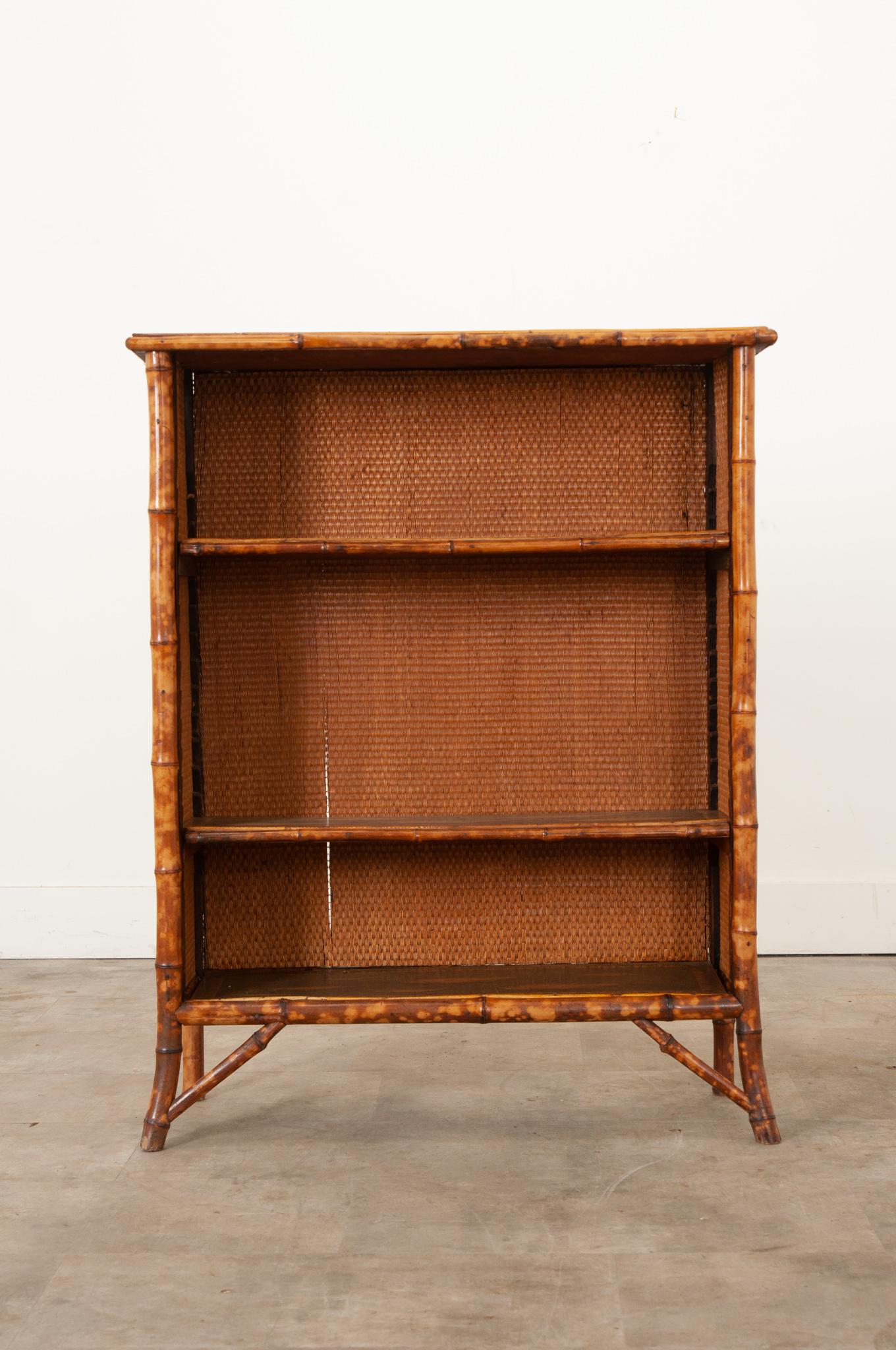 A 19th century bamboo bookcase with seagrass panels and fish motif decoupage details. The interior has two adjustable shelves at 9 1/2”deep.  The front legs are splayed outward, adding not only to the stability of the piece, but also creating a more