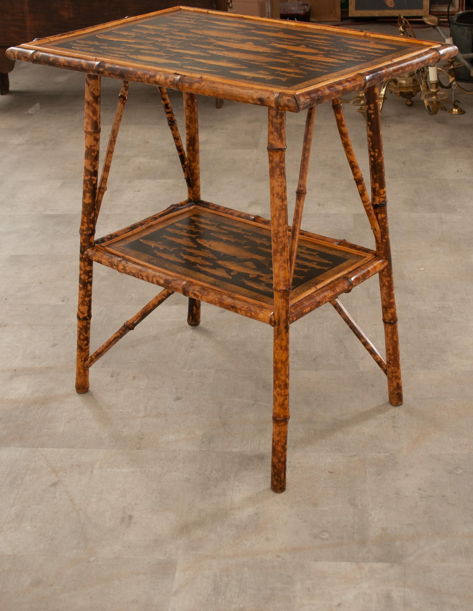A darling English two tier side table, circa 1890. Crafted from deeply toned bamboo that has been refinished with black paint, overlaid with brilliant decoupage paper fish and an intricate Greek Key style trim which have been aged perfectly to match