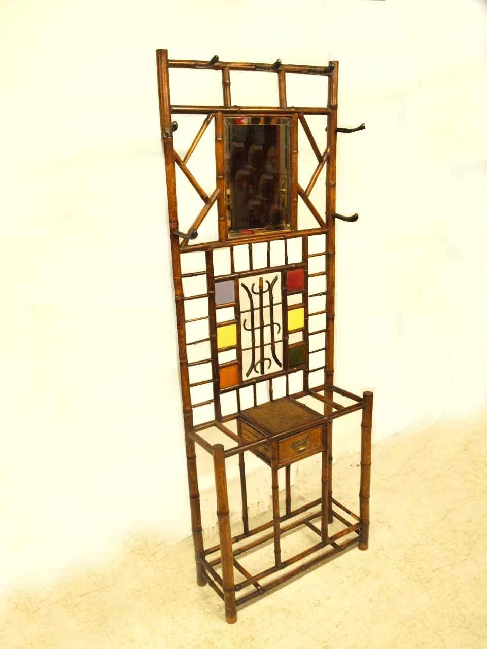 English bamboo hall stand with original steel hat hooks in simulated bamboo design, original beveled glass mirror, middle portion with multicolored tiles surrounding creative bamboo centerpiece; lower portion with single drawer.