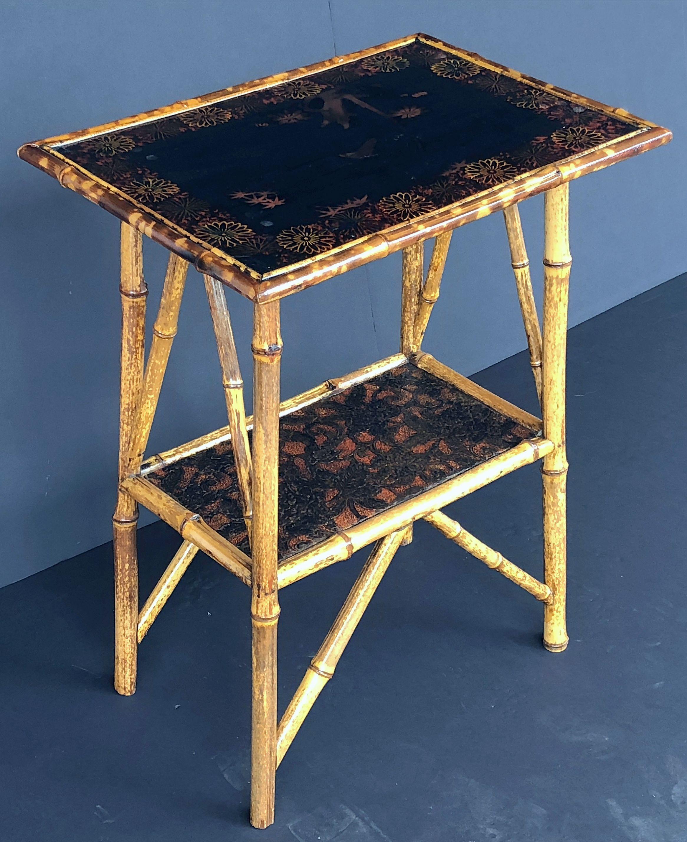 A fine English bamboo table (side or occasional) featuring a rectangular top with Japan lacquered chinoiserie design, over a stretcher base with rectangular pressed paper design panel and ornamental fretwork running diagonally at each corner.