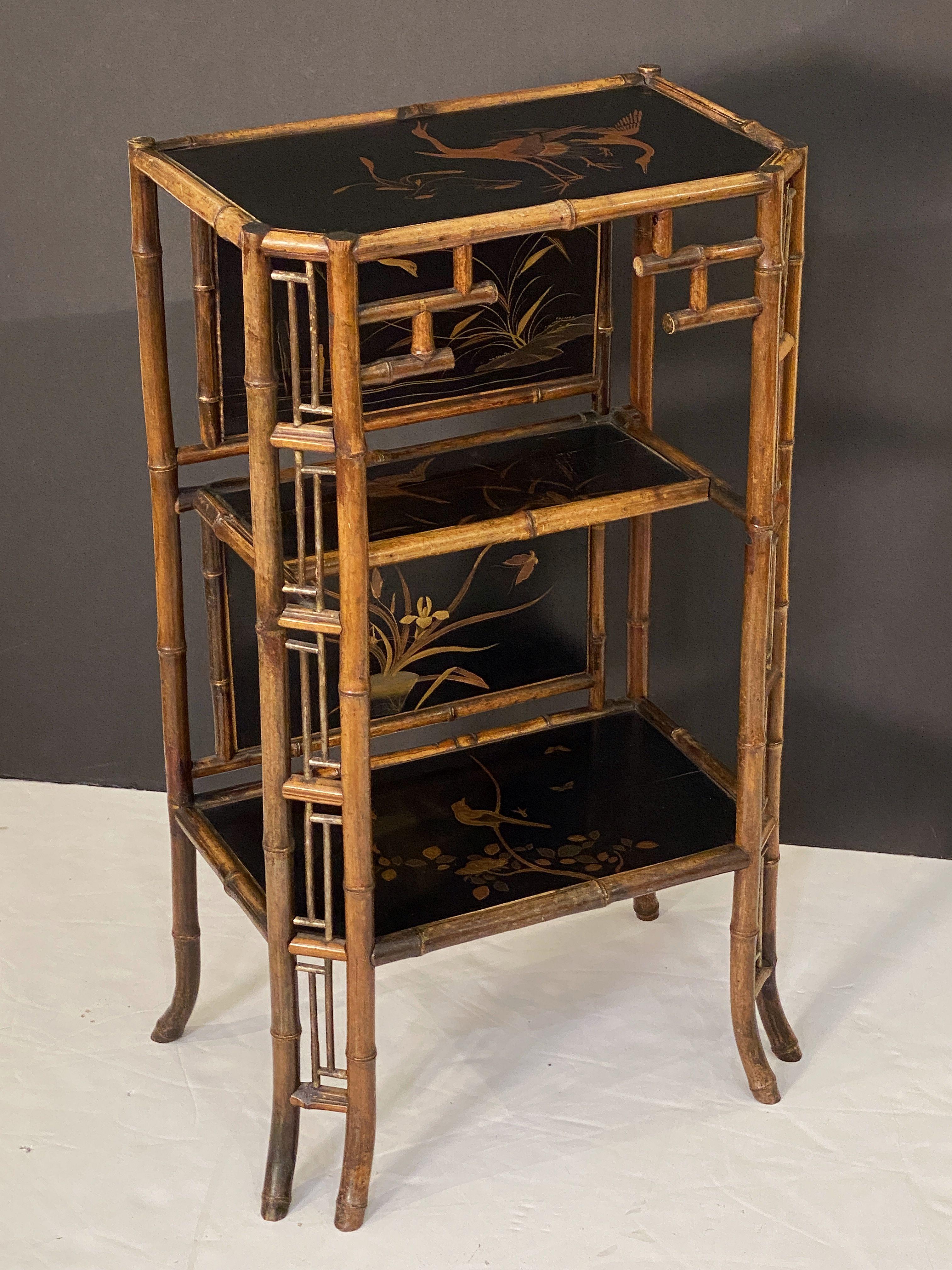 A fine collector's quality English bamboo table stand or etagere shelf cabinet from the Aesthetic Movement period, circa 1870-1910, featuring a rectangular canted top with Japan lacquered chinoiserie design, over a stretcher base with two shelves
