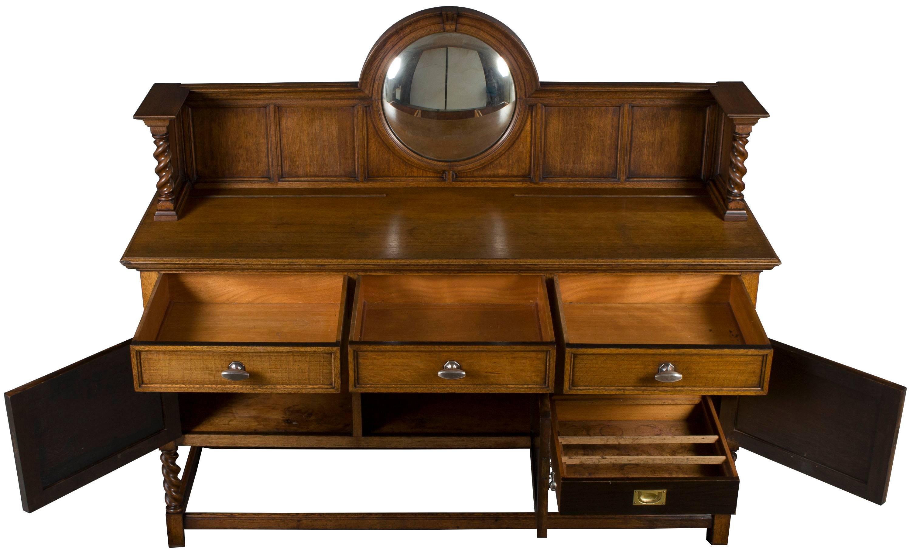 This unique English sideboard was crafted circa 1940 of oak. The oak has a light, honey color to it. Gorgeous turned barley twist is featured on the legs and back splash supports. A round convex mirror on the back splash is a unique touch as well.