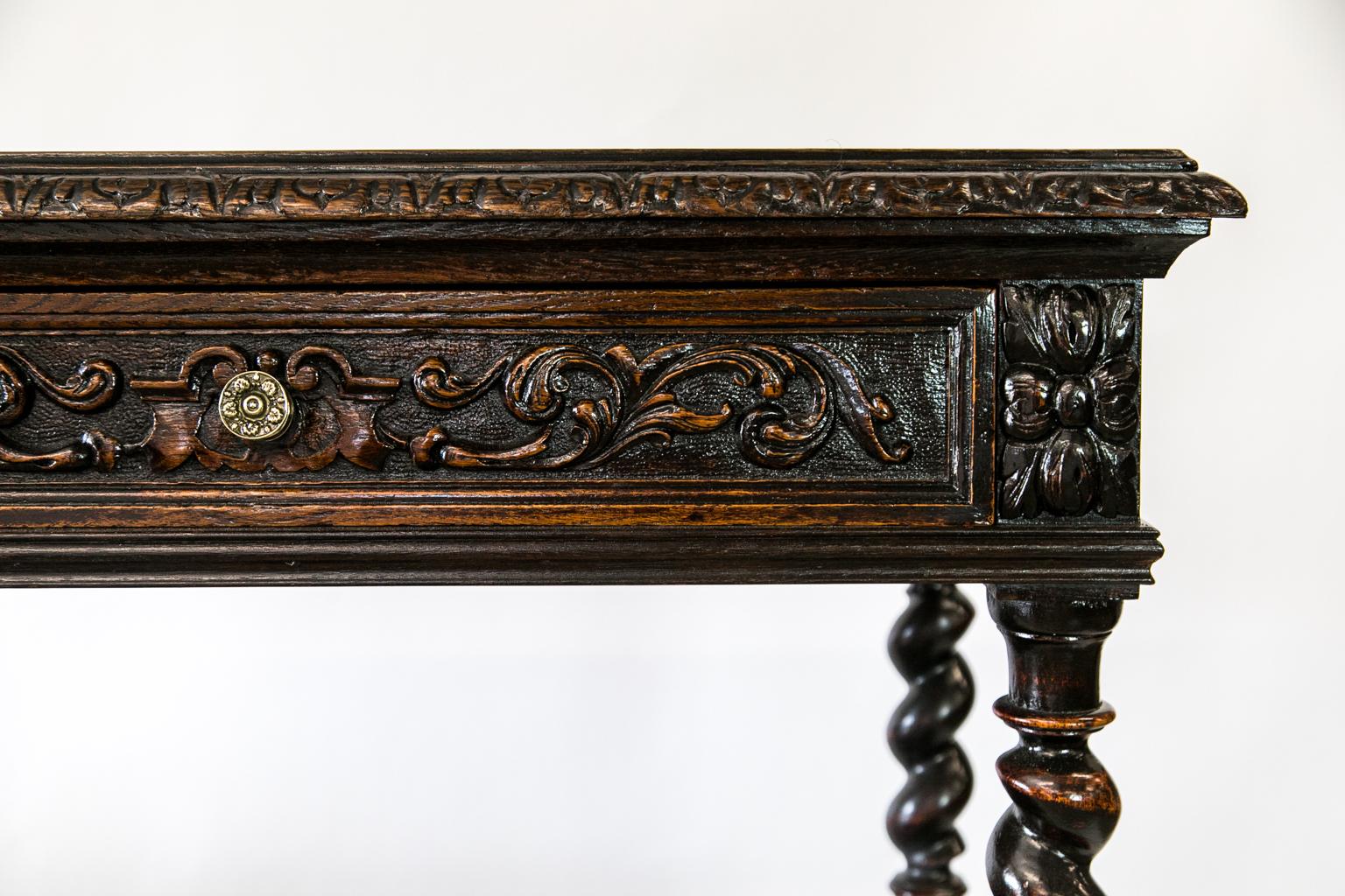 This English oak two tiered server/cabinet has heavy carved top molding. The drawer has floral arabesques carved in high relief. The lower cabinet door has leaf, vine, and fruit carvings, and carved bell flower swags on the lower stiles. The top