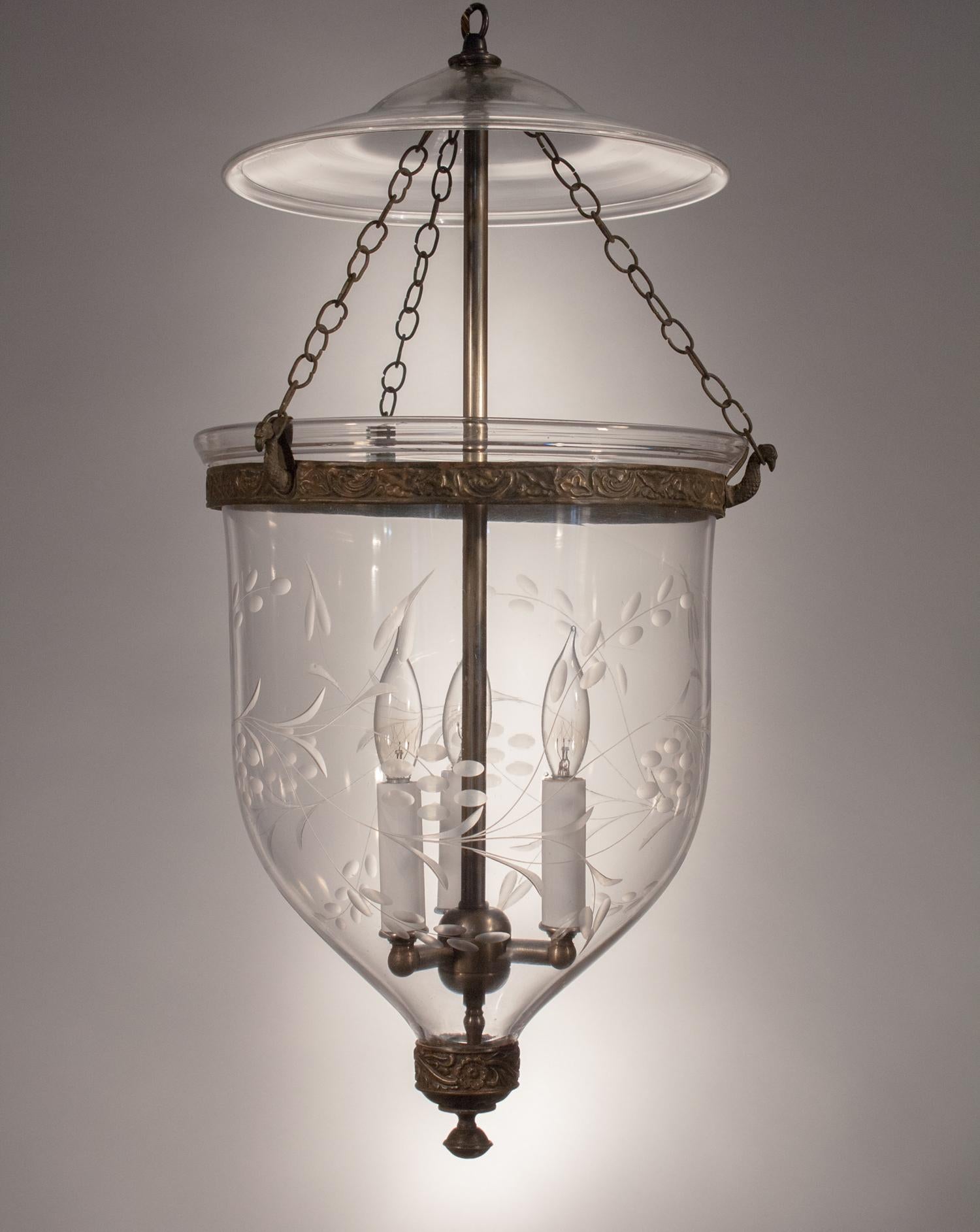 This hand blown glass bell jar lantern features its original smoke bell, brass candleholder base, band, and chains. It has a truly beautiful form that is complemented by a graceful, etched vine motif. The lantern has been newly electrified with a