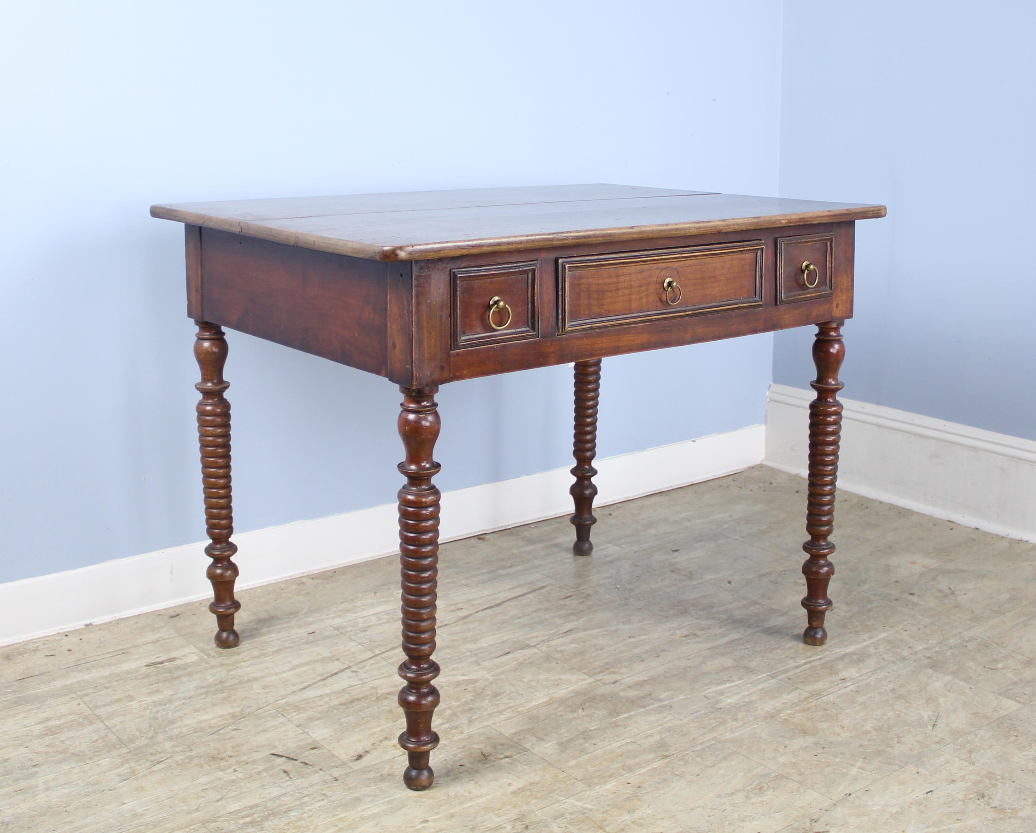 An early turned leg side table, generously proportioned with a single center drawer and two faux front drawers on either side. Very good walnut color and patina on the top. The base is most likely fruitwood. There is a separation of the planks at