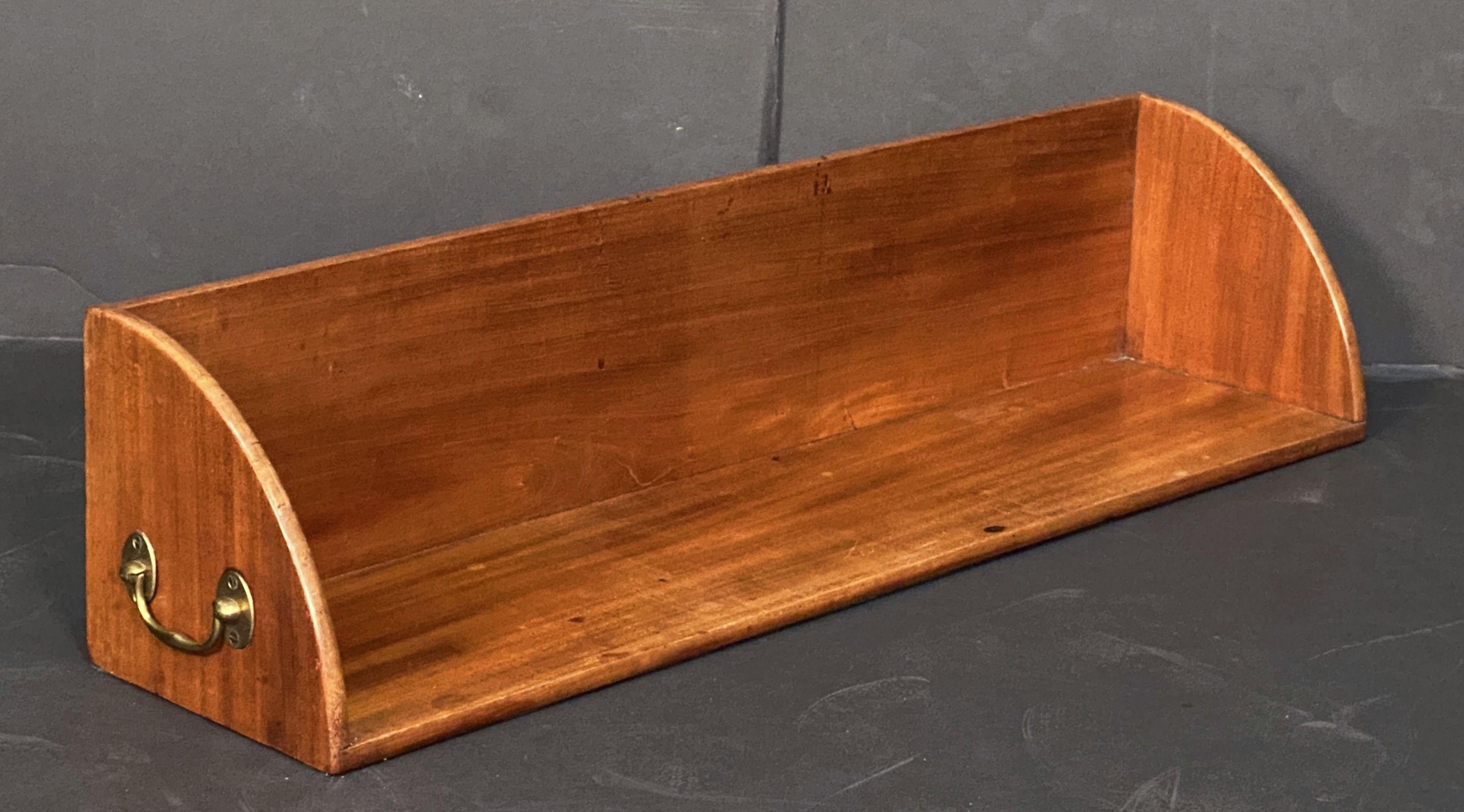 A fine English table top book rack or library stand (trough) or mahogany, from the late 19th century, featuring a novel design with original brass lifting handles on opposing ends.



