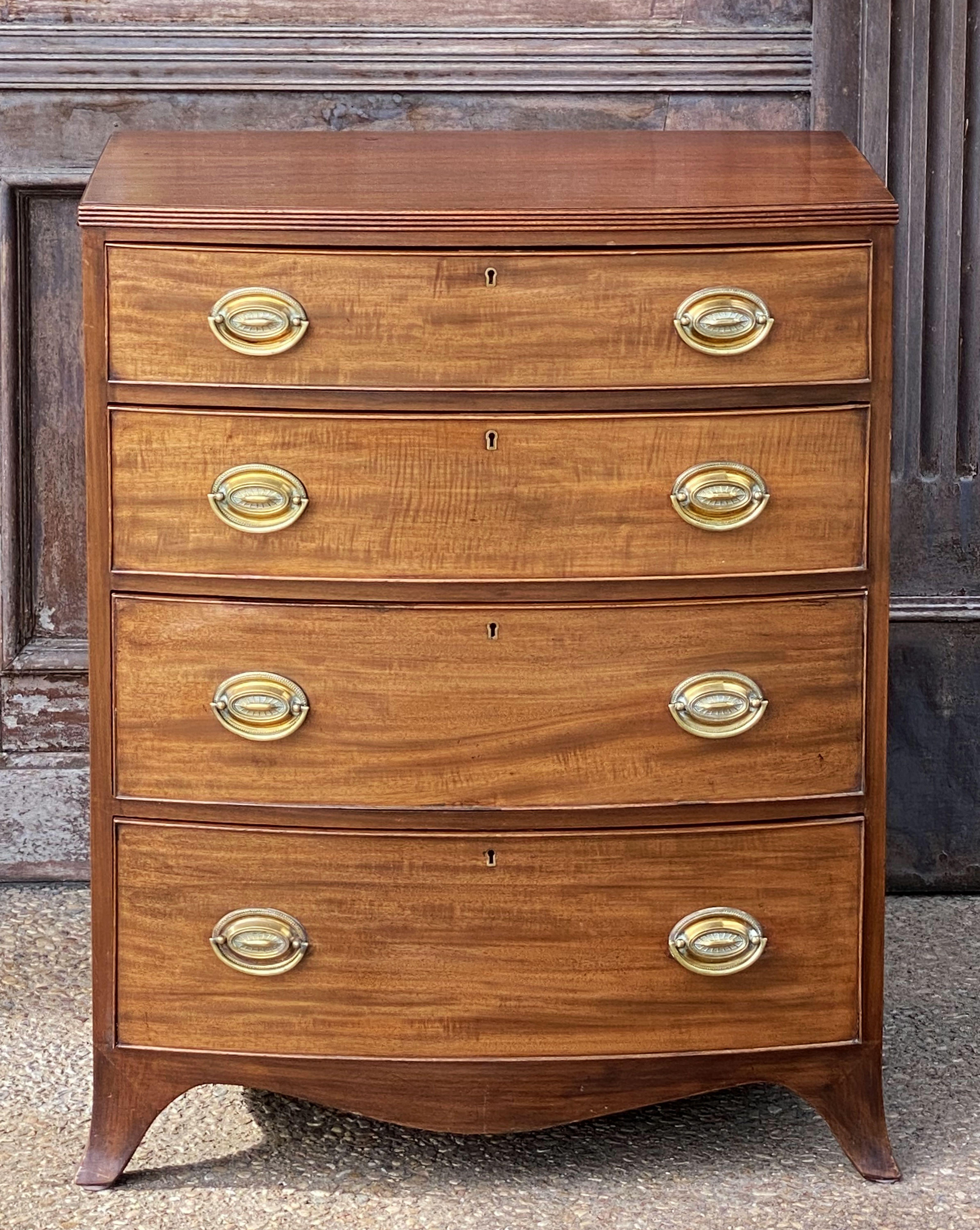 A handsome English bow-front chest of drawers of mahogany from the 19th century - featuring a bowed top over a frieze of four beaded drawers, each drawer with fine flame-cut mahogany veneers, brass handle pulls, and brass escutcheons, set upon a