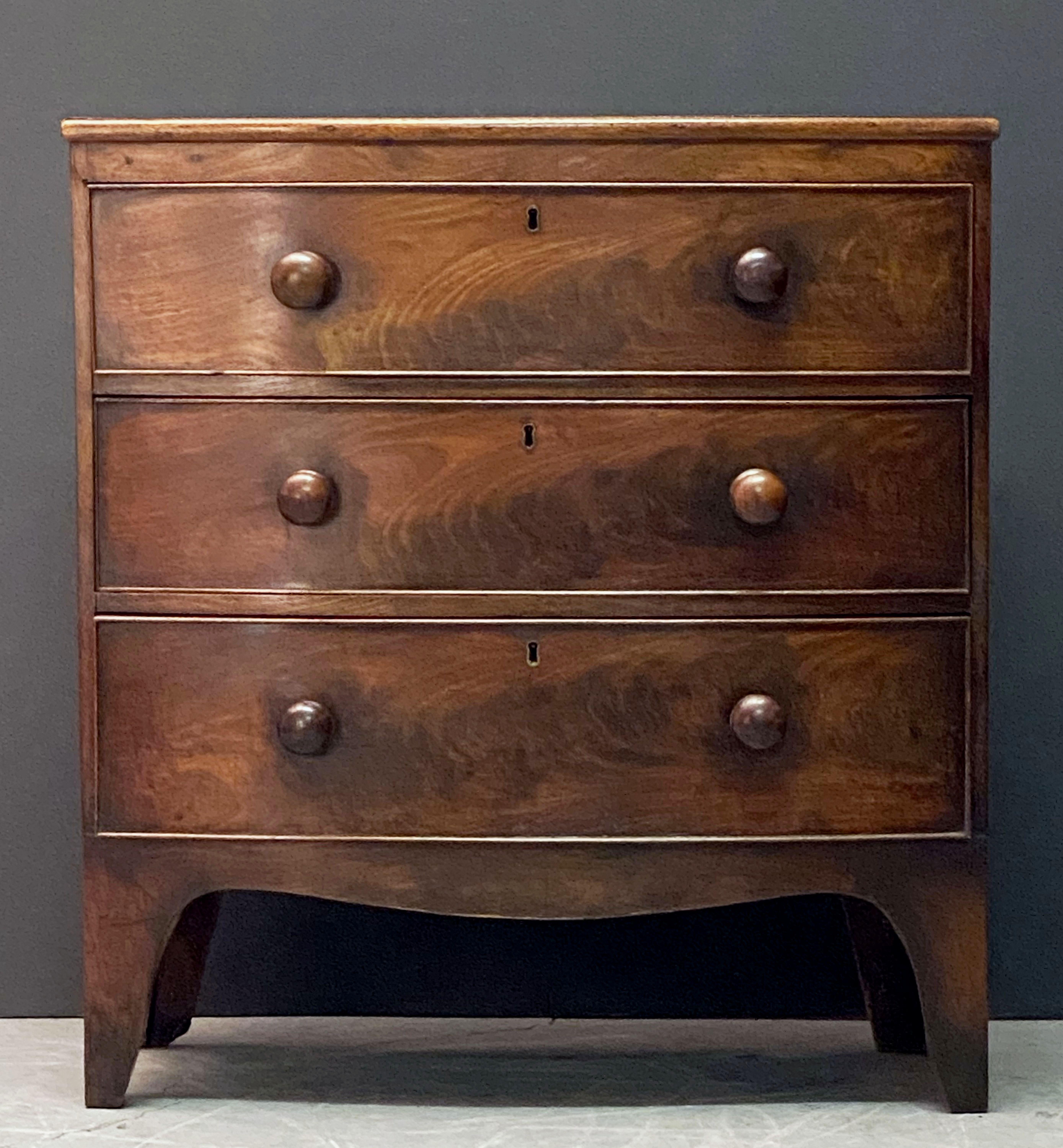 A handsome English bow-front small chest of drawers of mahogany from the 19th century - featuring a bowed top over a frieze of three beaded long drawers, each drawer with fine mahogany veneers, knob pulls, and brass escutcheons, and set upon a