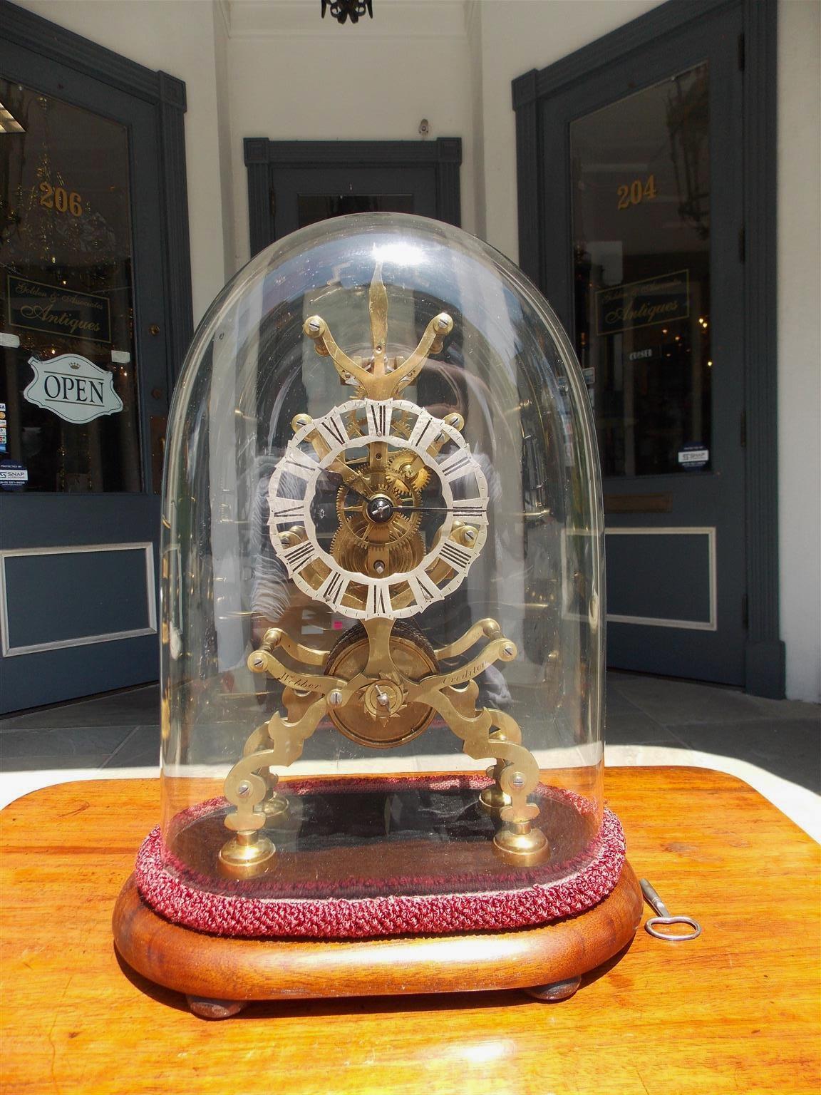English brass skeleton clock under original glass dome with a polished steel roman numeral dial, fuse chain movement, and affixed to an oval carved wood felt base with four bun feet. Stamped Webber, Town of Credition. Late 19th century. Clock is in