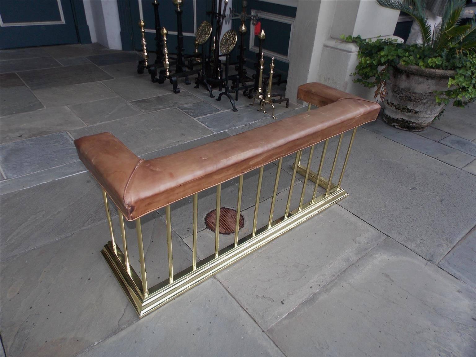 English club fender with tan leather seat, brass vertical supports, and resting on a molded edge base. Mid-19th century.