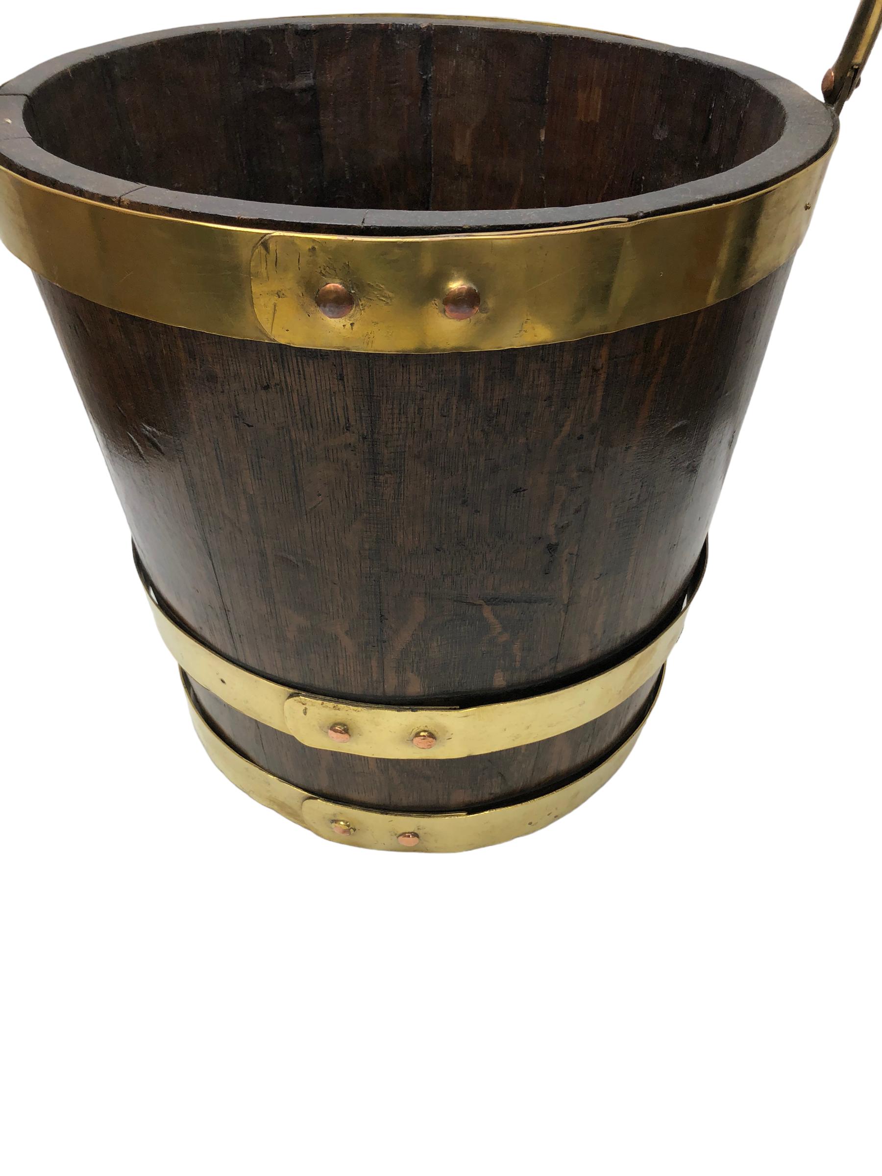 English Brass Bound Oak Peat Bucket.  Early 20th Century oak bucket bound by three brass bands. Heavy brass handle pivoting handle. Coopered and staved construction. Well patinated. Originally used to store turf or peat, now used as a kindling