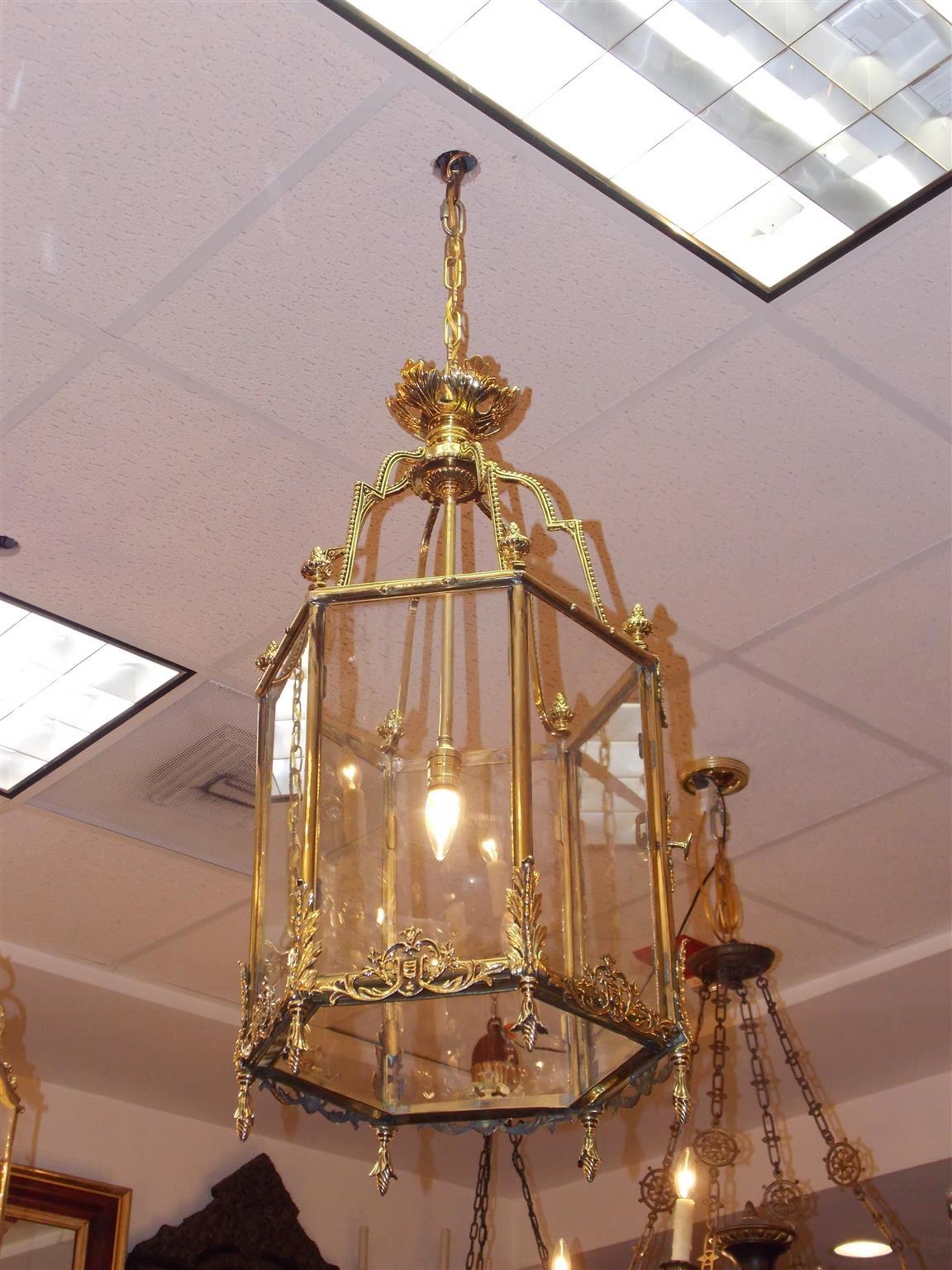 English brass hanging hall lantern with a floral canopy,  scrolled step back beaded arms adorned with bulbous finials, six floral decorative glass panes with a hinged locking door, single interior light, and each corner resting on decorative