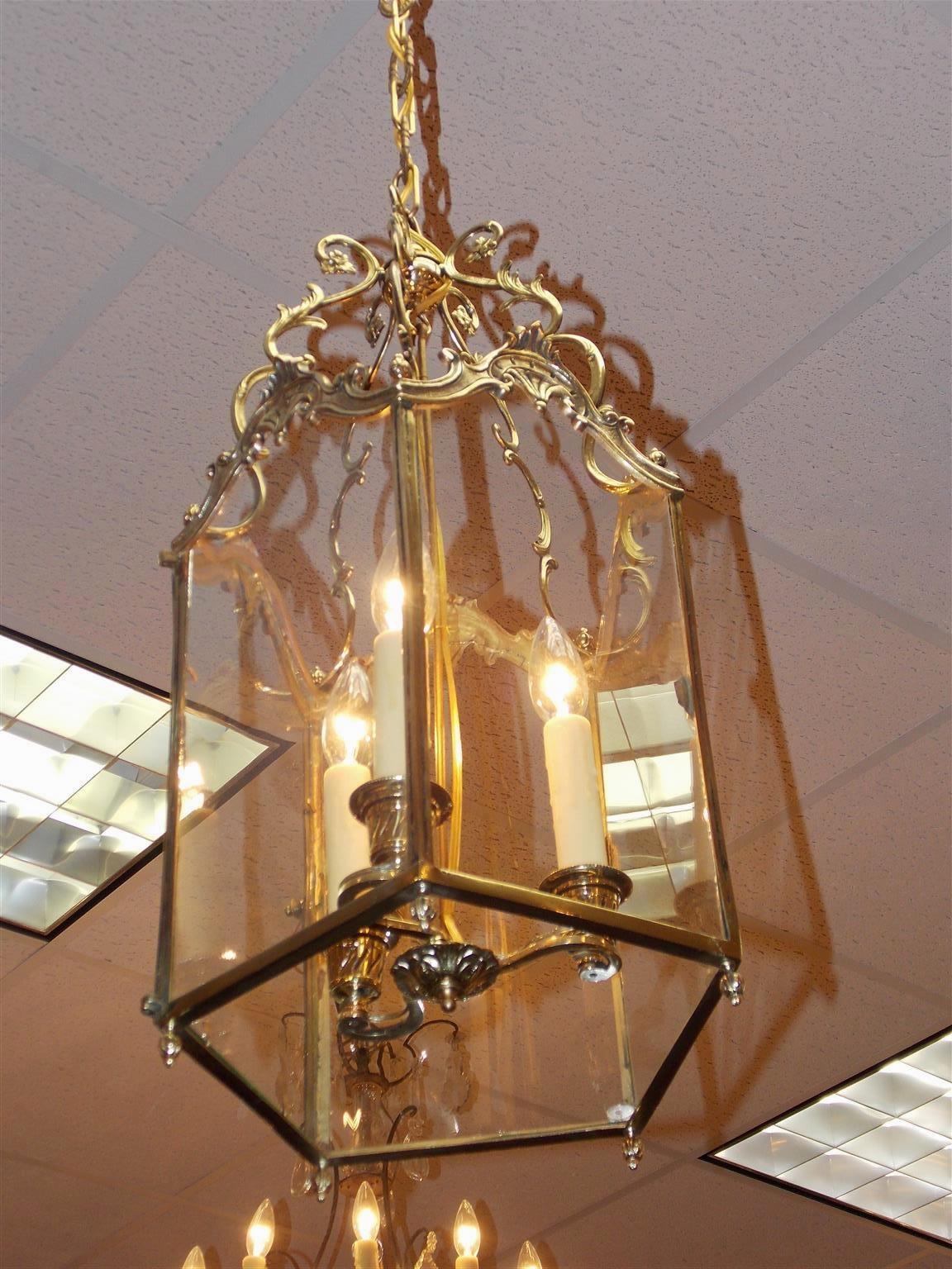 English brass hanging hall lantern with scrolled floral arms, five arched floral glass panes, hinged locking door,  interior three light cluster, and resting on floral bulbous finials. Originally candles and has been electrified, Early 19th century.