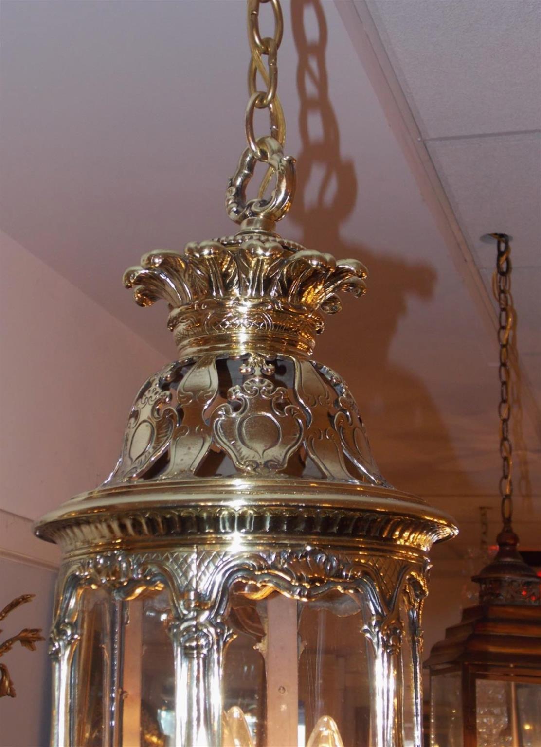 English brass hexagon hanging hall lantern with a decorative centered ring over Prince of Wales plumes, bulbous chased pierced dome with a filigree border, single hinged locking door, interior three light cluster with the original gas piping, and