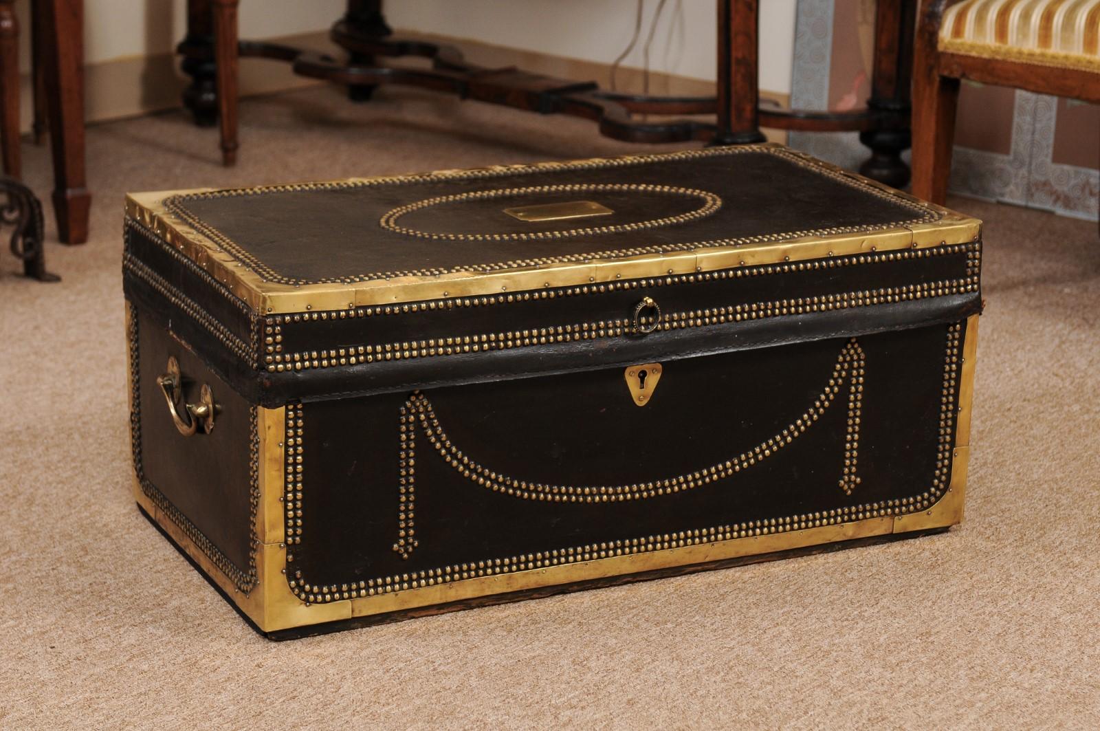 The English brass mounted and studded black leather trunk with swag detail and side handles. The interior in camphor wood. 

 