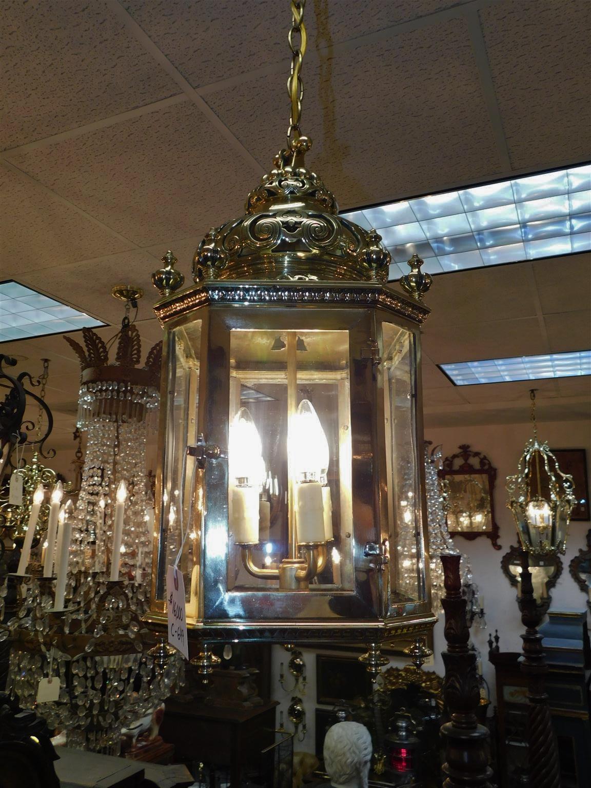 English brass octagon hanging hall lantern with a decorative chased and pierced two tiered bulbous beaded dome, paneled glass with a single hinged door, eight upper floral finials with a filigree border, three light interior cluster, eight lower