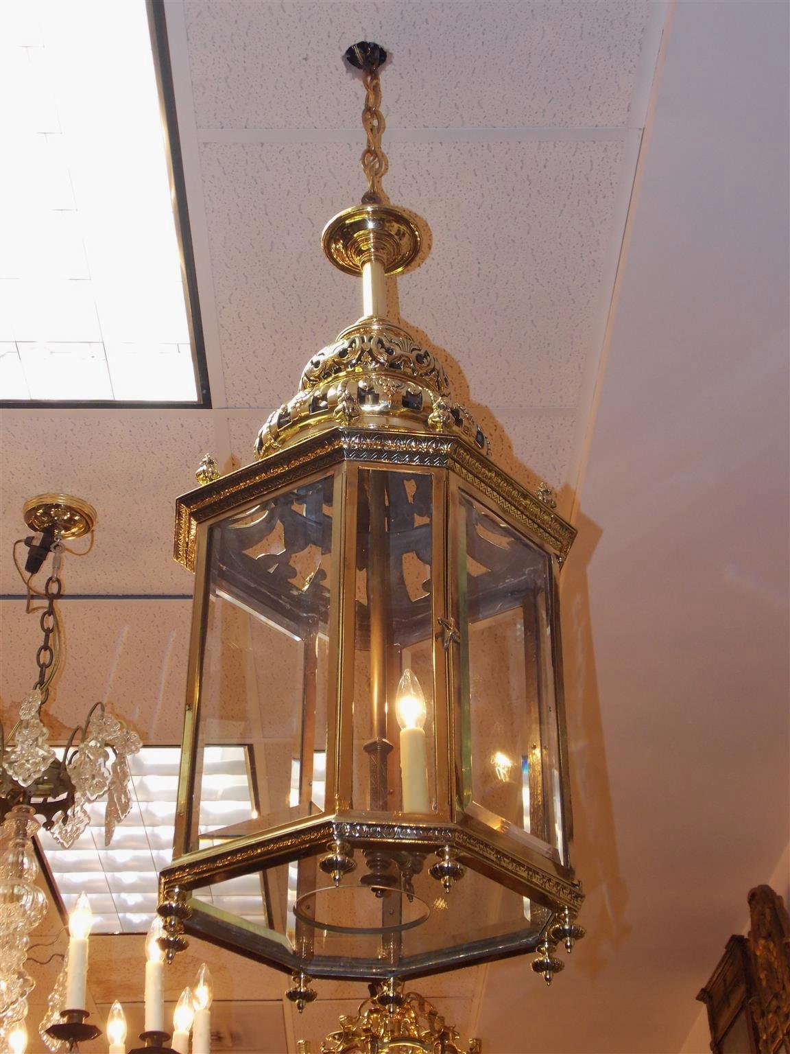 English brass octagon hanging hall lantern with a decorative centered bulbous two tiered beaded, chased, and pierced dome, beveled paneled glass with a single hinged door, eight upper floral finials with a filigree border, two light interior cluster