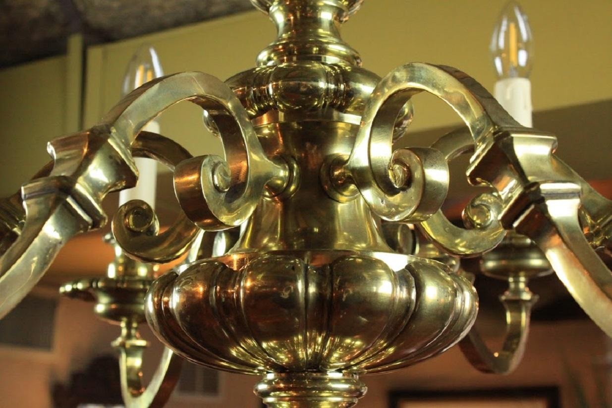 English brass chandelier with ball and looped top above a lobed vase shaped stem. Six scrolling arms with knobbed centers. Stem is finished with orbs and a finial.