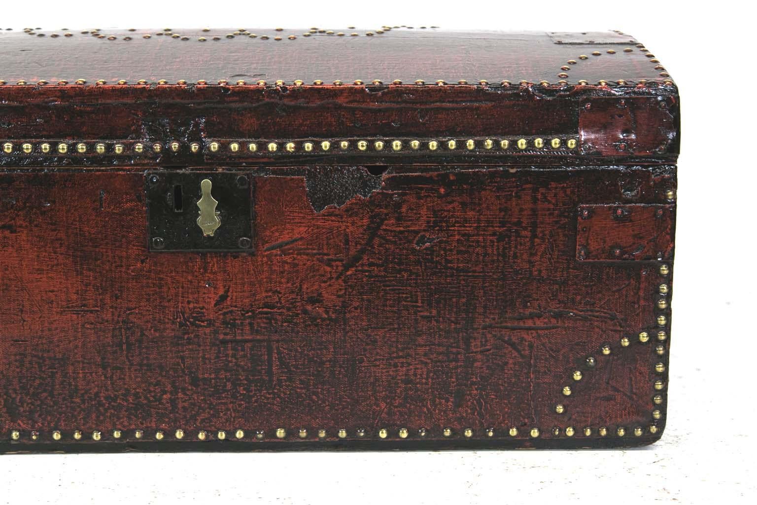 English brass studded painted trunk has steel support strapping and the original steel carrying handles. It appears that the original covering is leather which has been painted and antiqued. There is a patented brass key hole escutcheon mounted to