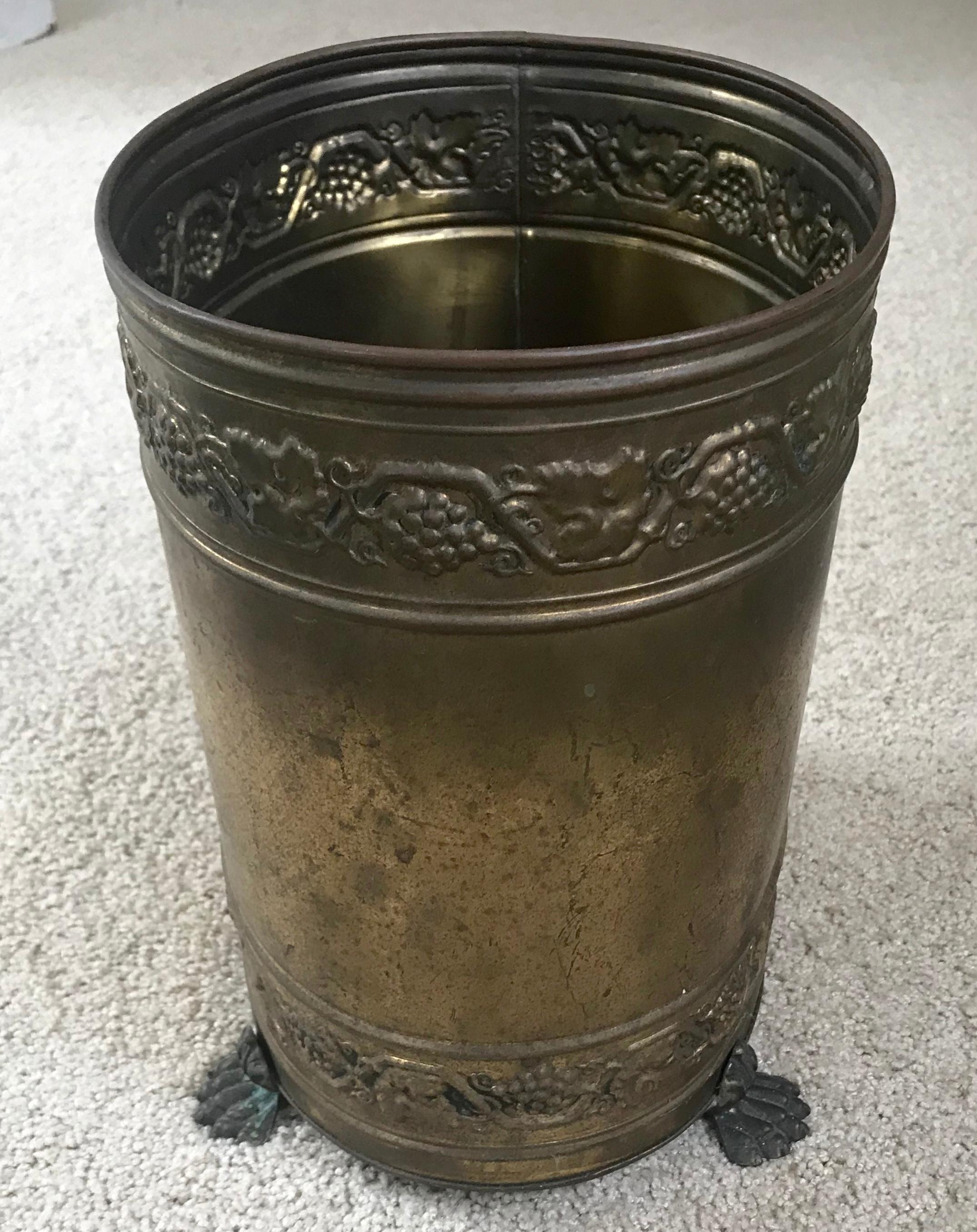 English brass wastebasket on paw feet. Vintage patina oval brass litter basket with scrolling grapevine banding at top and bottom resting on four claw feet. England, mid-20th century.
Dimensions: 10.75” H x 10” L x 7.75” D.