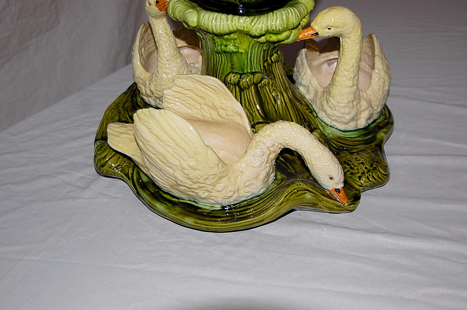 English Bretby Majolica centerpiece in two parts. There are three full bodied swans with wings spread so plants or food or other decoration can be placed within their bodies, they are swimming around a central column of leaves which support a
