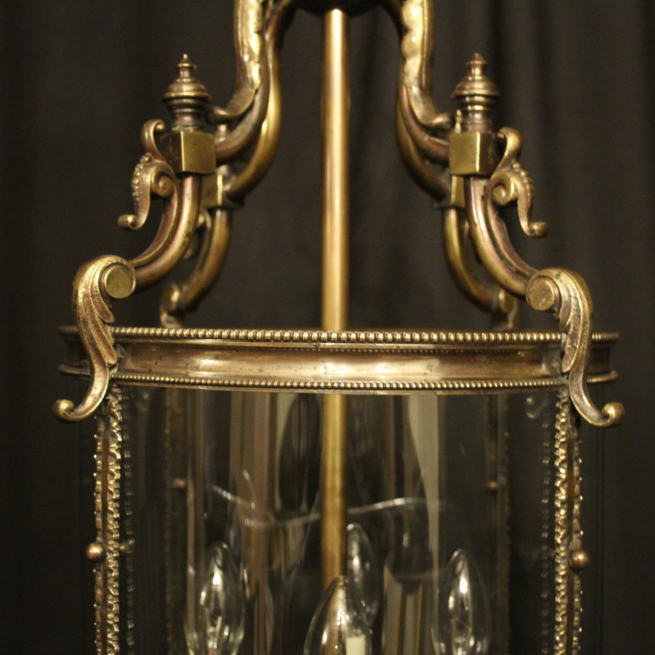 A large English cast bronze four-light antique hall lantern, the four arms with millgrain candle sconces, surrounded by four sectional circular convex glass panels and held within a scrolling framework with side imbricated leaf panels and open