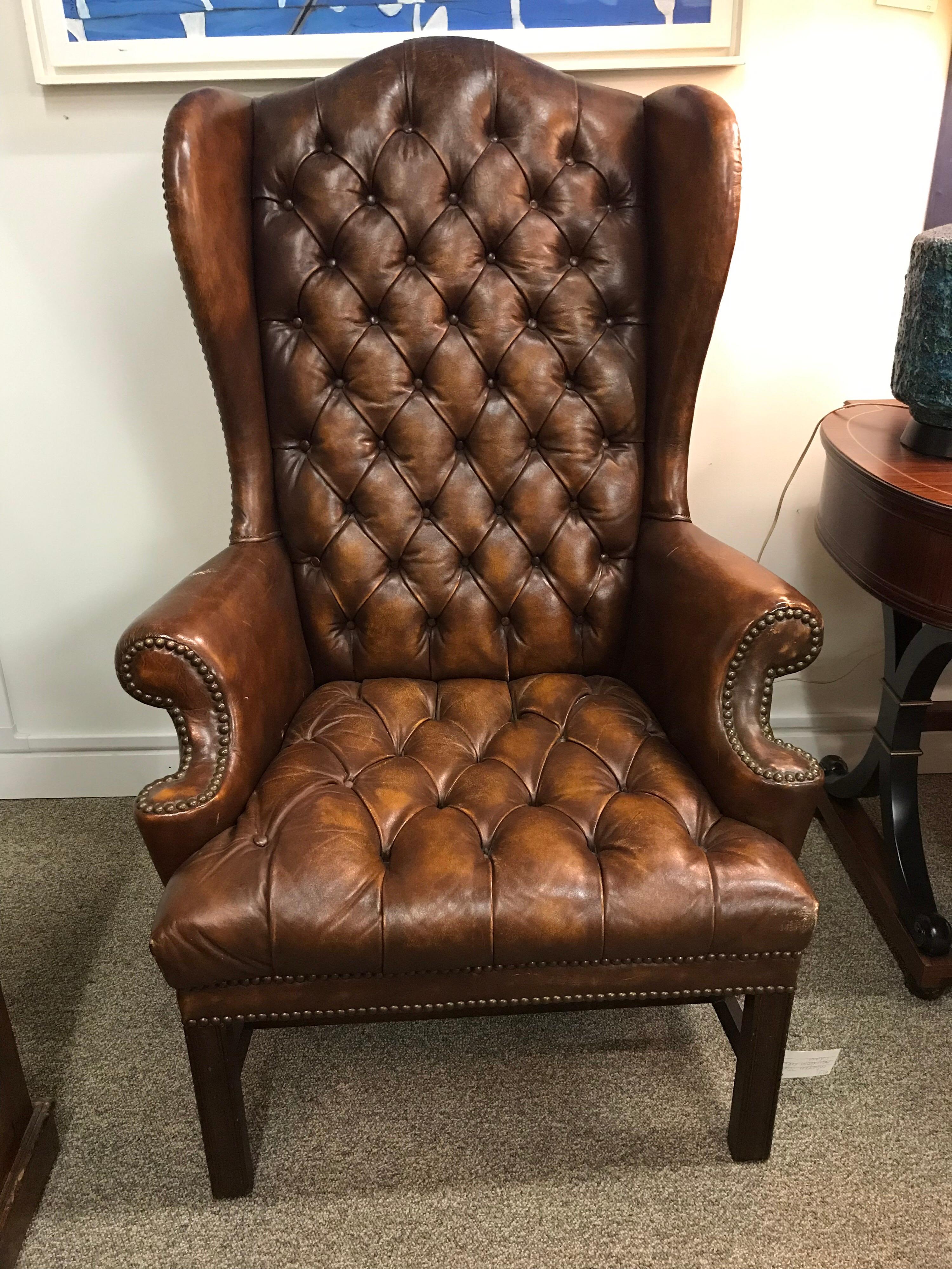 English Chesterfield leather wingback armchair is button tufted on back and seat. Original leather upholstery has desirable distressed patina from years and years of use. Finished with brass nailhead trim all around.