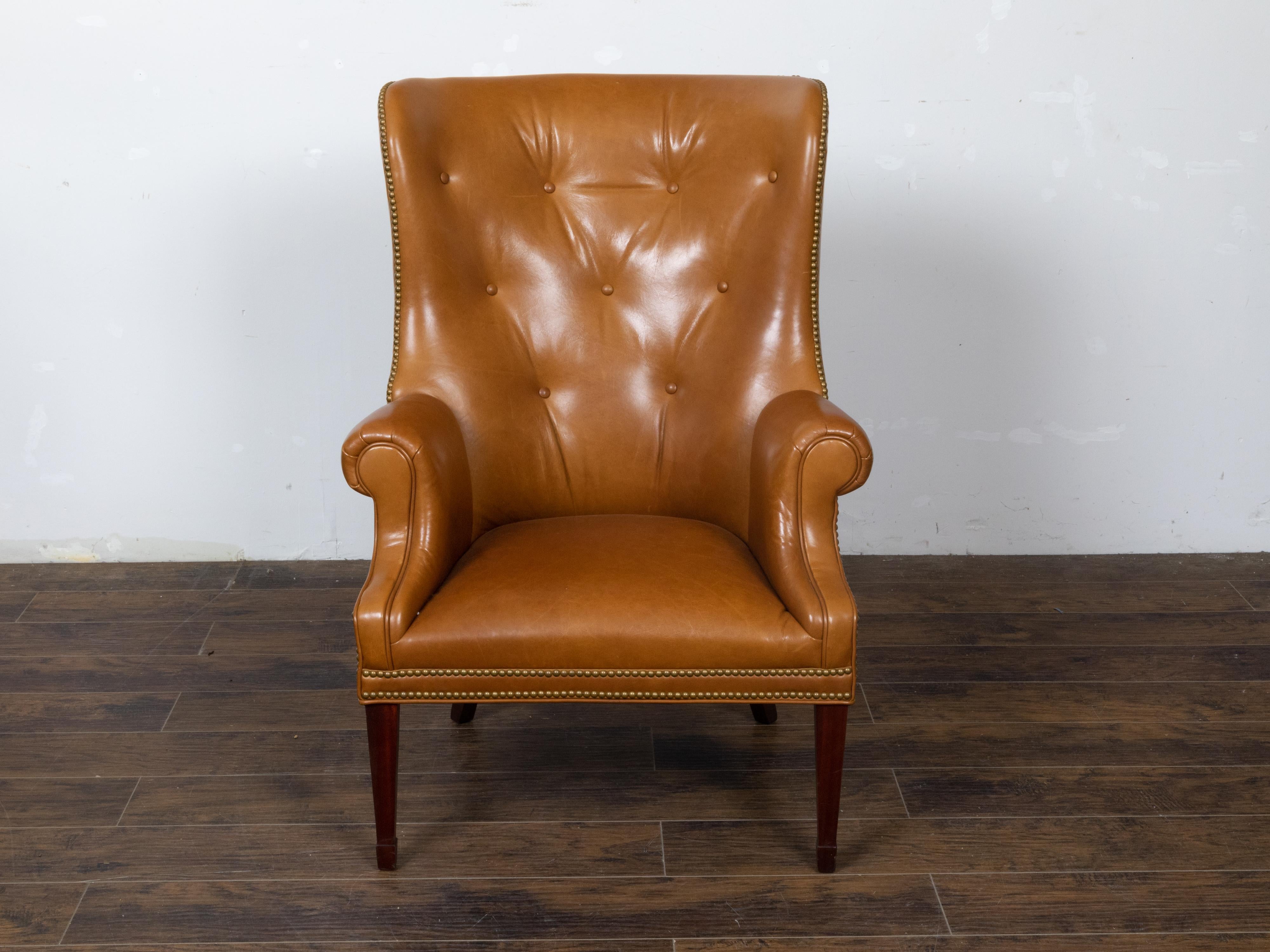 An English brown leather wingback chair from circa 1930-1940 with brass nailhead trim, tapered legs in the front and saber legs in the back. Step into the epitome of classic comfort and timeless style with this English brown leather wingback chair,