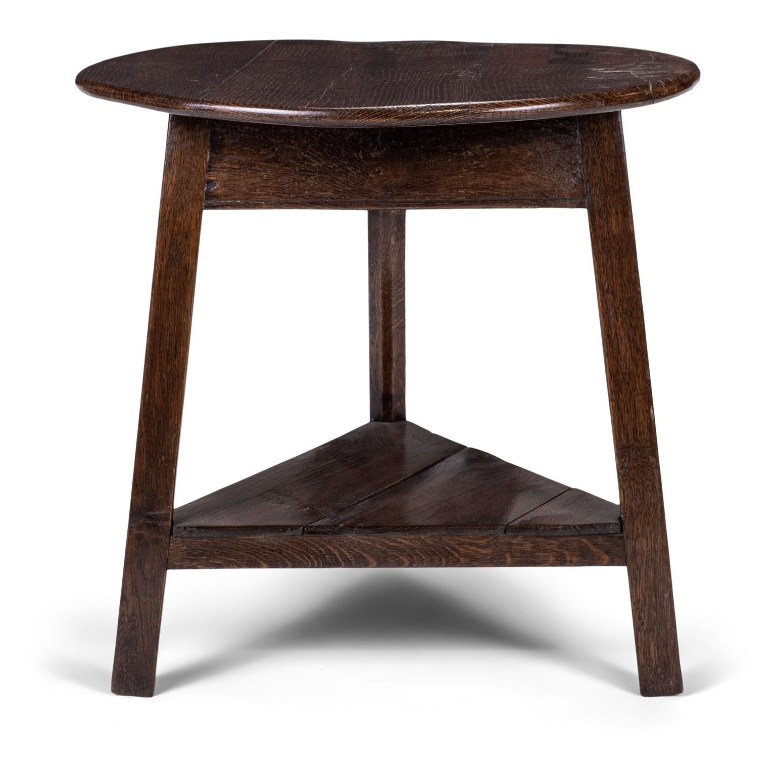 Early 19th century English brown oak cricket table of typical form. Circular top raised on three splayed legs united by an under tier shelf. Sturdy, stabile mortise and Tenon construction.
