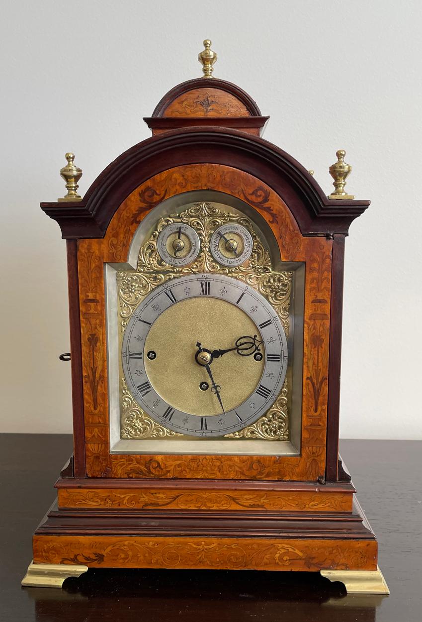 An English Burl Wood Musical Mantel Clock, circa 1880 in the Georgian Style - This imposing clock with break arch case profusely decorated with floral inlay, surmounted by an arched pediment and with five brass finials, glass break arch panels to