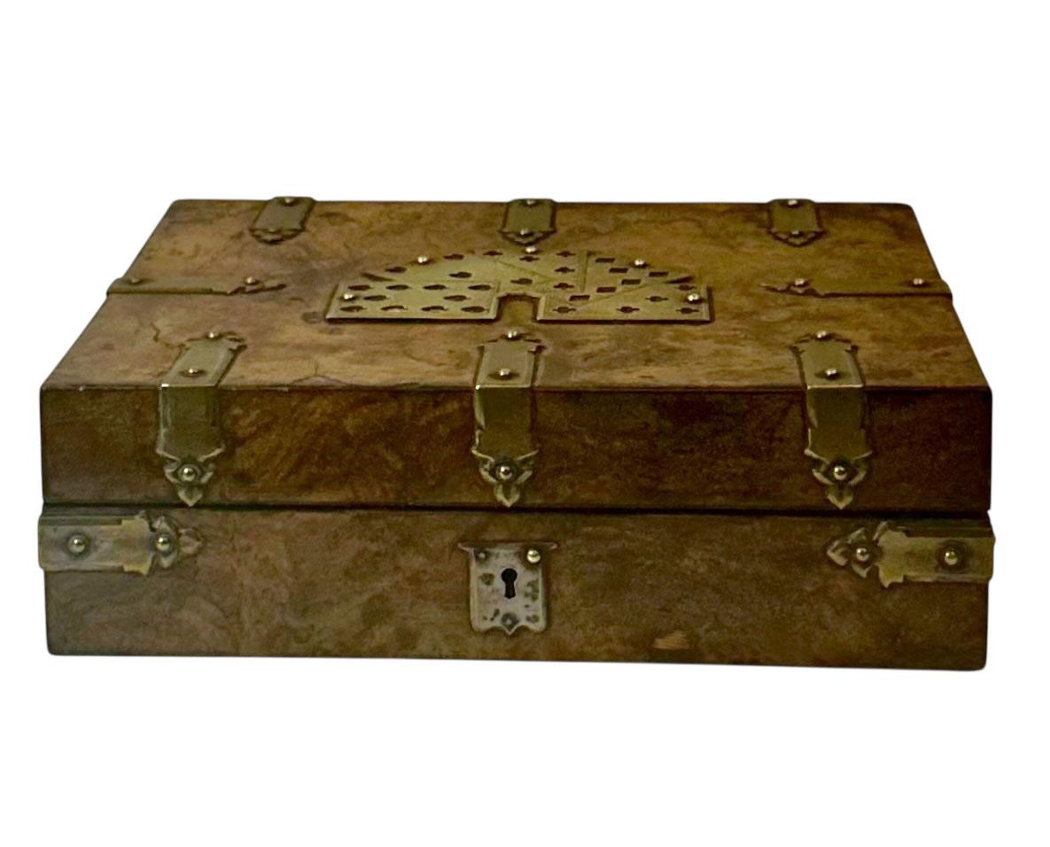 Scatola per carte di metà Ottocento, in legno di radica inglese, finemente lavorata e riccamente ornata da dettagliati supporti in ottone e da un affascinante motivo di carte da gioco sul coperchio. Questo squisito cofanetto è caratterizzato da
