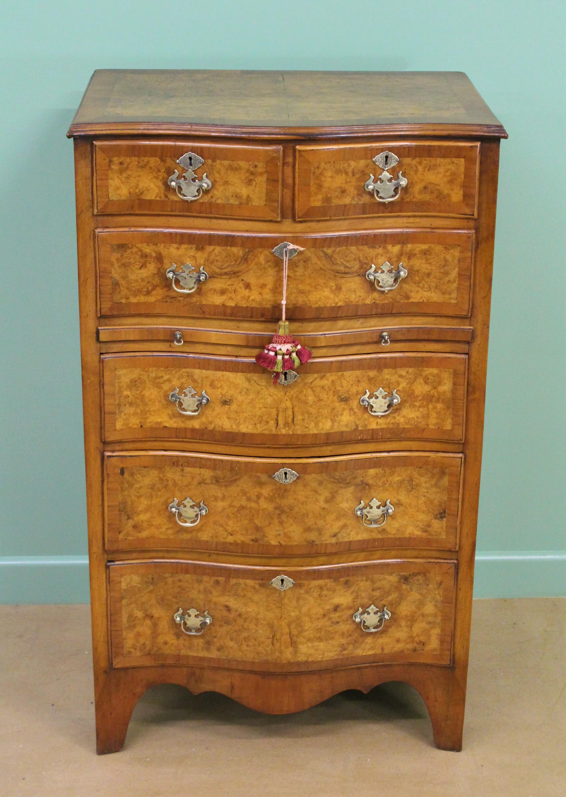 A charming burr walnut serpentine fronted chest of drawers. Well constructed in solid walnut with attractive burr walnut veneers. There is an arrangement of 2 short over 4 long, graduated drawers; and a brushing slide. The serpentine shaped top and