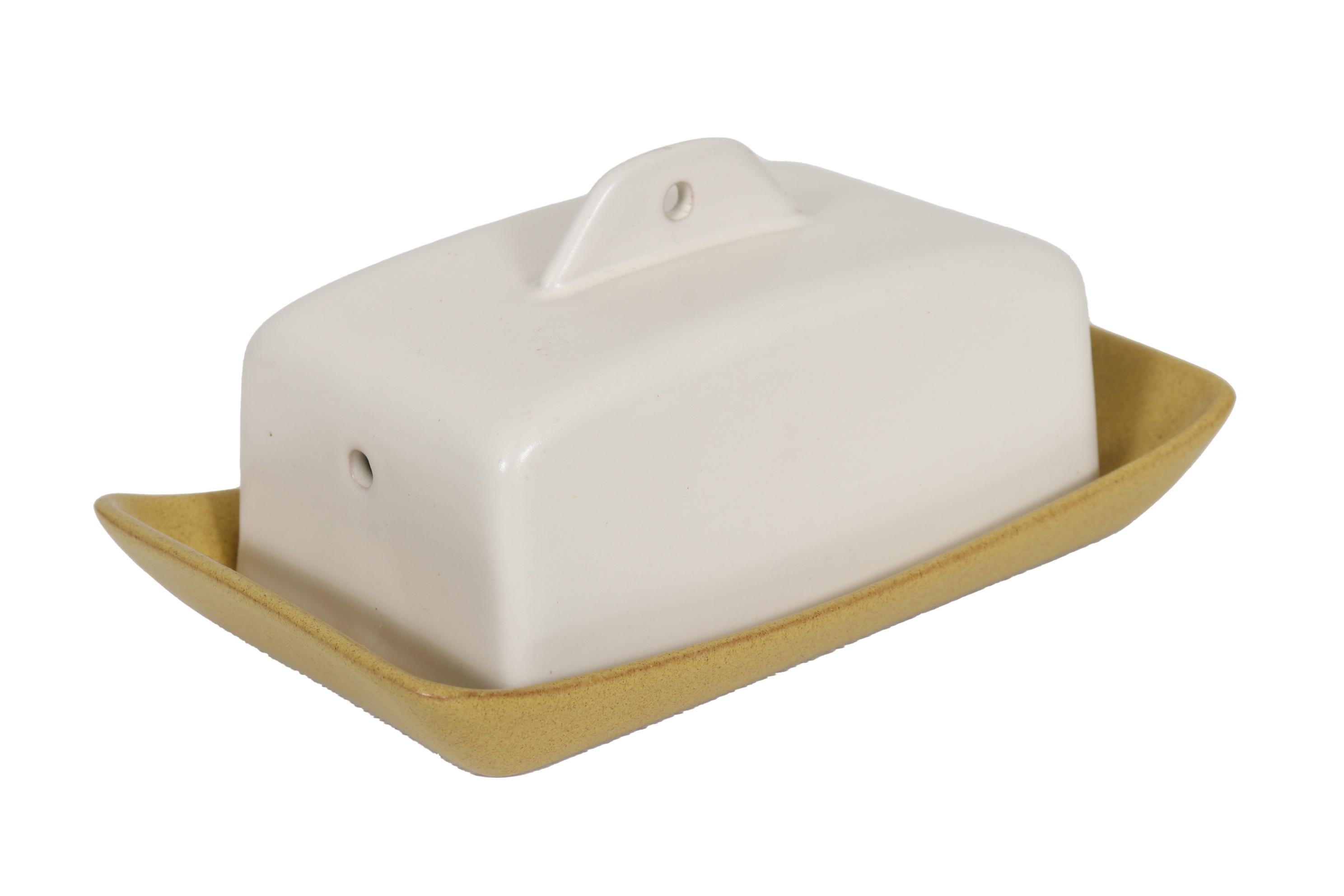 A modern earthenware English butter dish made by Denby, a traditional English pottery company in the village of Denby, Derbyshire. A traditional rectangular shape is modernized with sweeping curves and mustard and eggshell white hues. Marked Denby