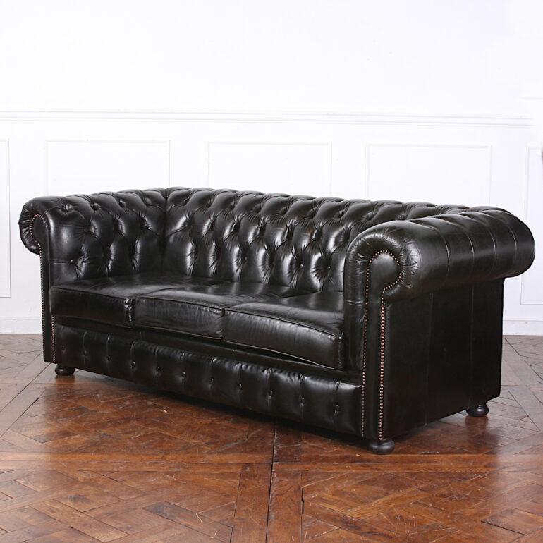 An English button-tufted black leather rolled arm sofa with brass stud details and simple turned bun feet. A handsome and comfortable example of this classic design and suitable for everyday use. 

Measures: 79? Wide x 34.5? Deep x 28.5? Tall