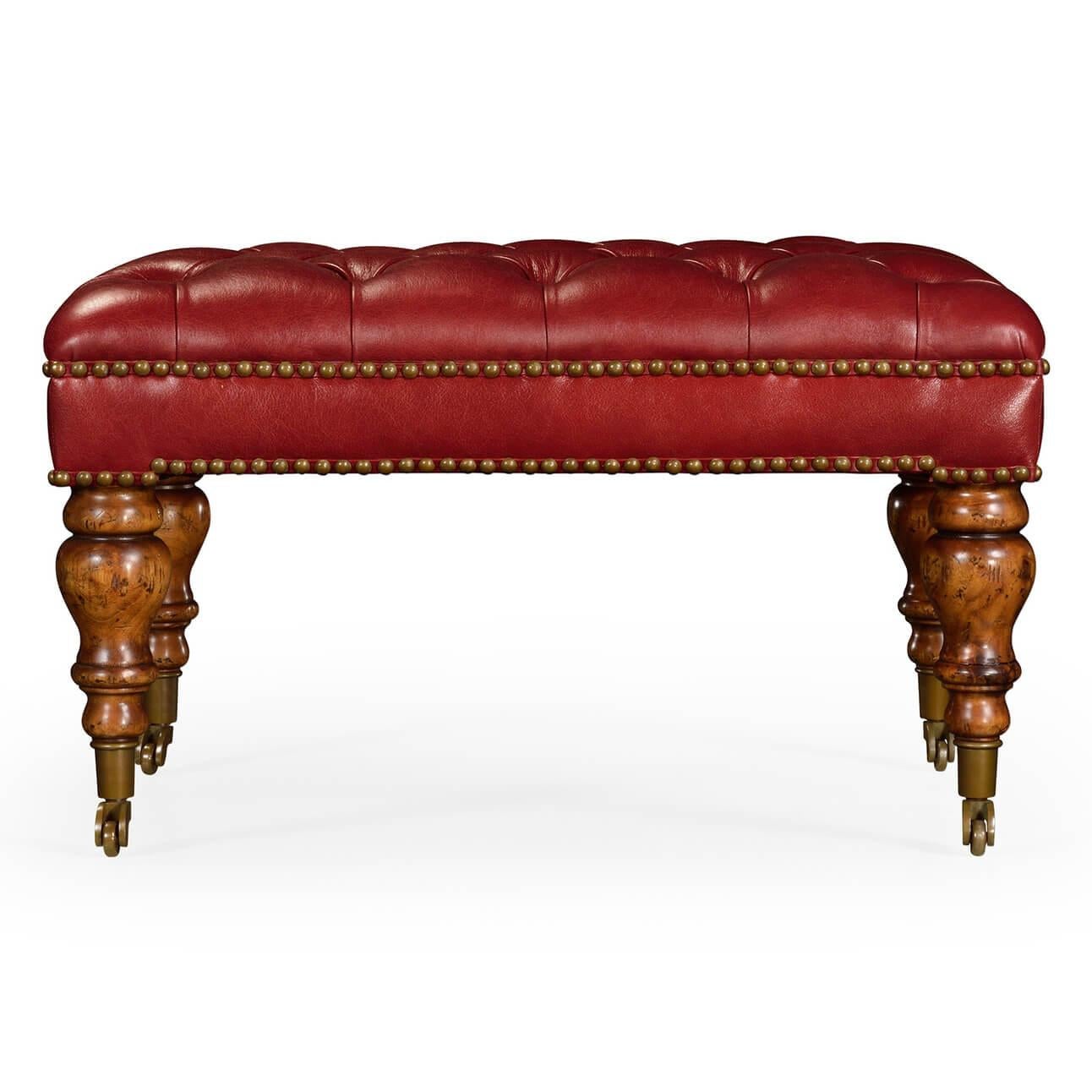 A large English Classic style leather upholstered, button-tufted footstool or ottoman with turned legs and brass casters.

Dimensions: 26.5