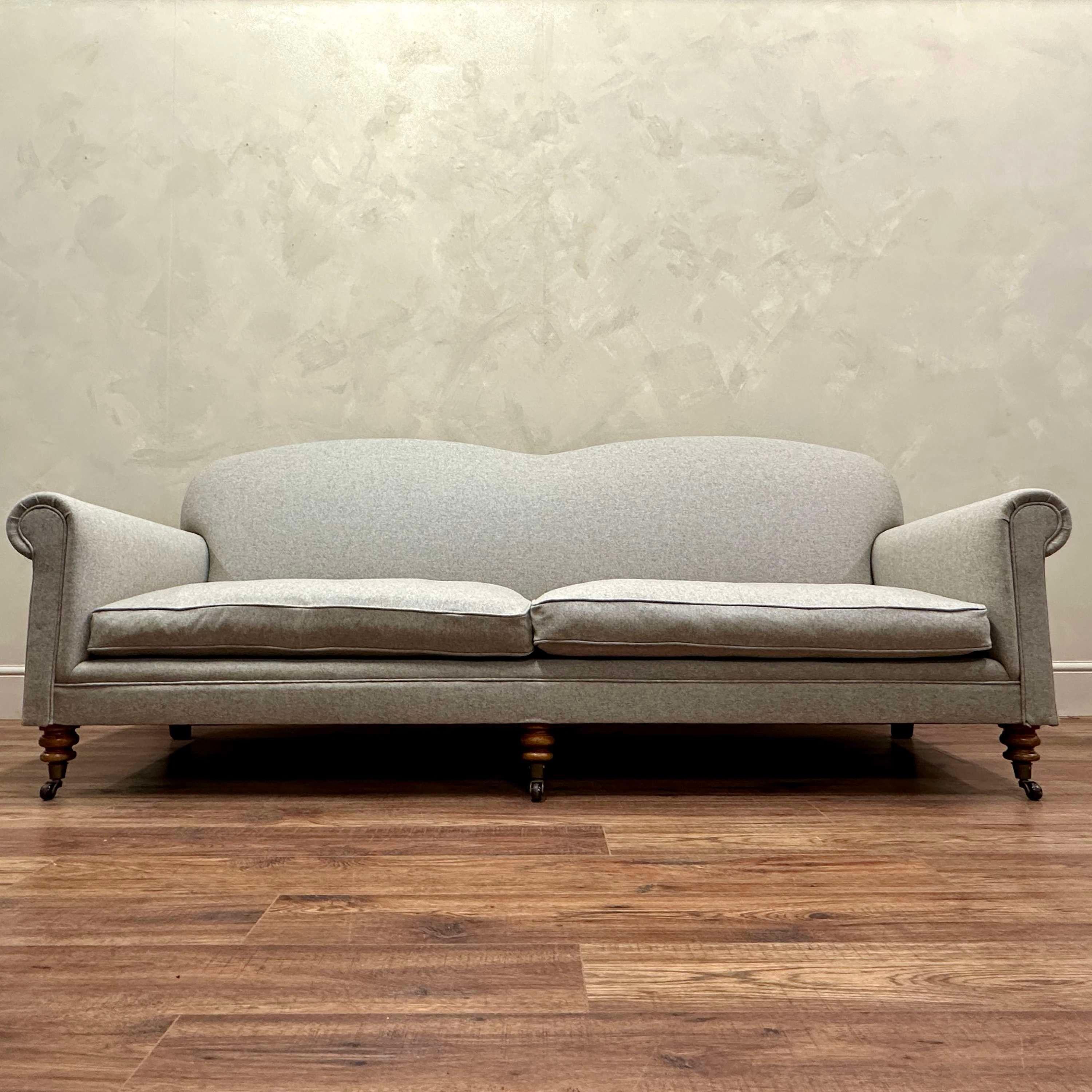 Large, Camel Back Sofa, upholstered in a soft-touch, plain Cotswold Wool in a grey/beige neutral which is fire retardant.
Deep filled feather seat cushions.
Resprung and webbed.
Original turned legs and casters.
England c 1900

Length: 220cm, Depth: