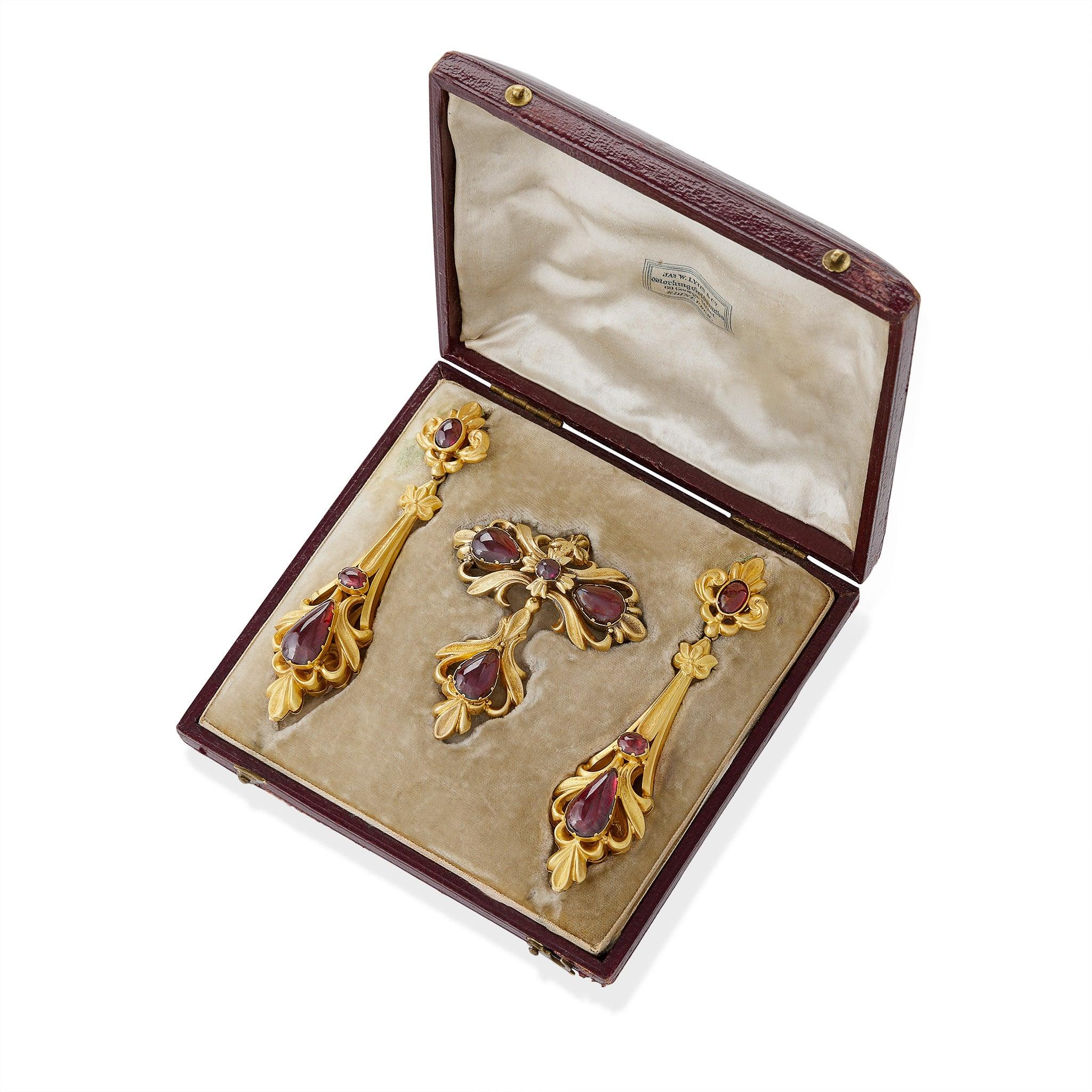 This antique Victorian 15K gold demi-parure comprising pendant earrings and pendant brooch with chain is set with over 10.00 carats of cabochon almandine garnets. The elongated pendant earrings are designed as scrolling leaf motif tops, each with an