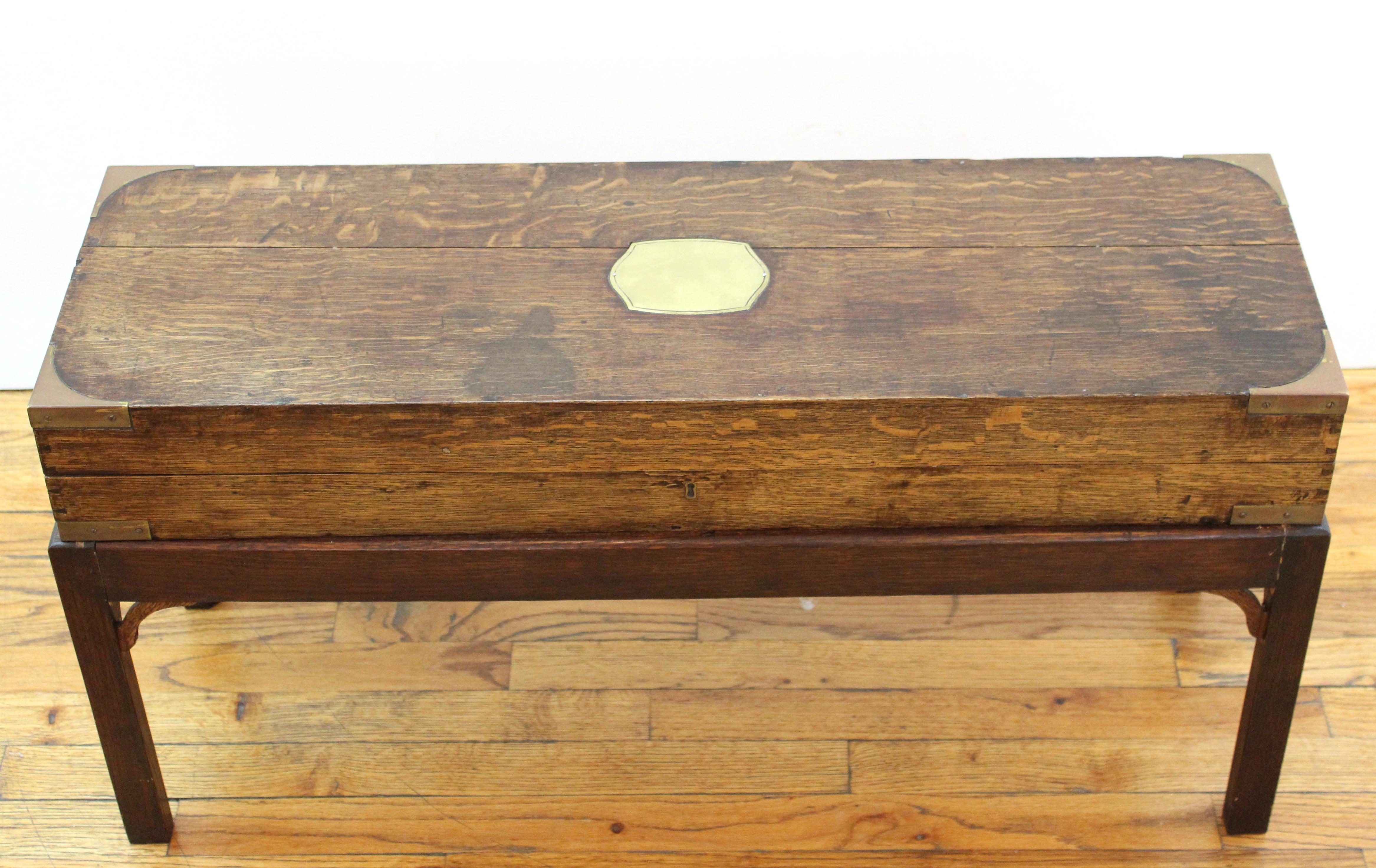 English campaign chest style storage box with brass inlay top, placed on pedestal legs, used as diminutive coffee table or cocktail table. Use and wear to the green felted interior.